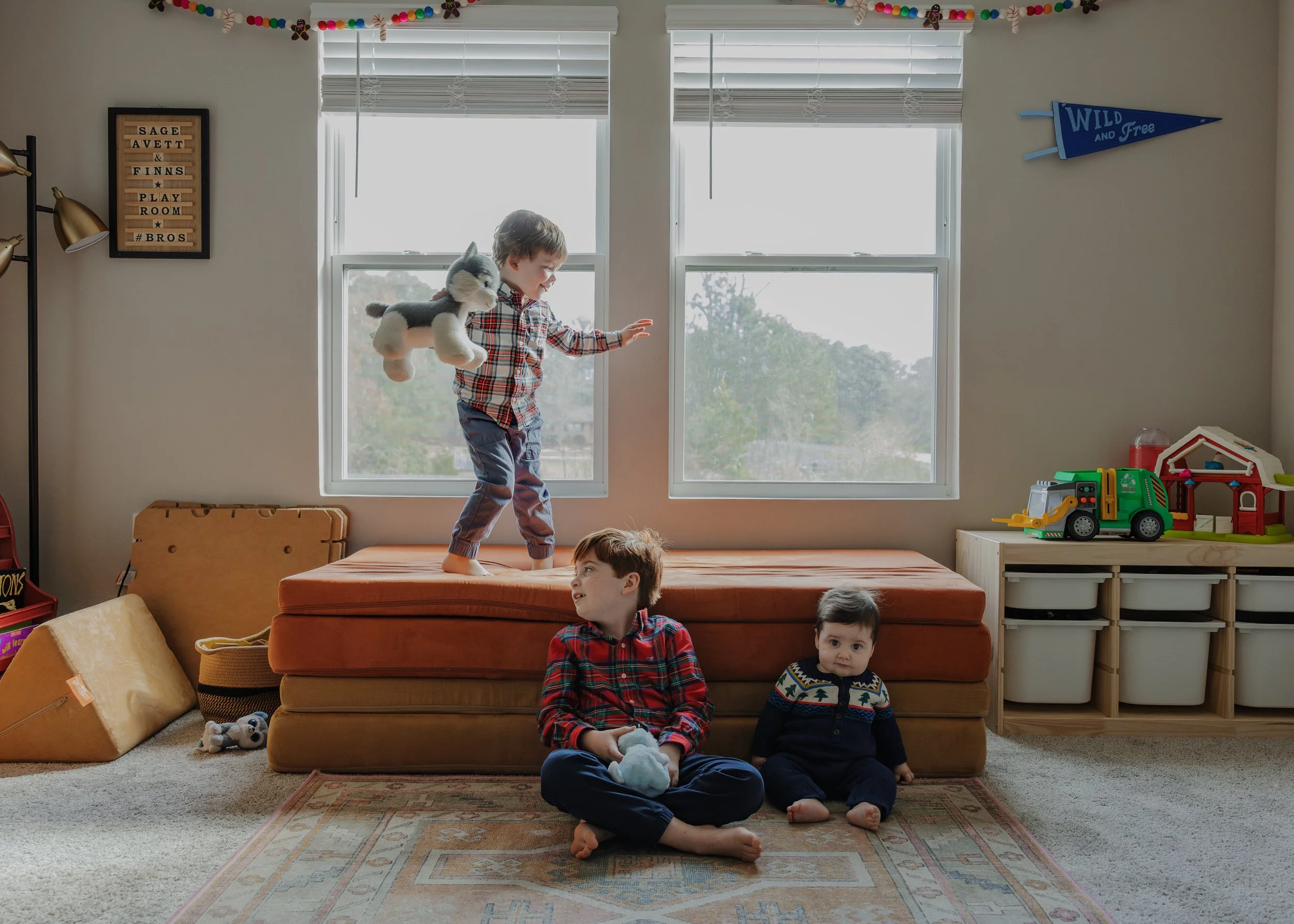 Brothers play with stuffed animals on their nugget couch during a lifestyle family photography session captured at home in Raleigh, NC.
