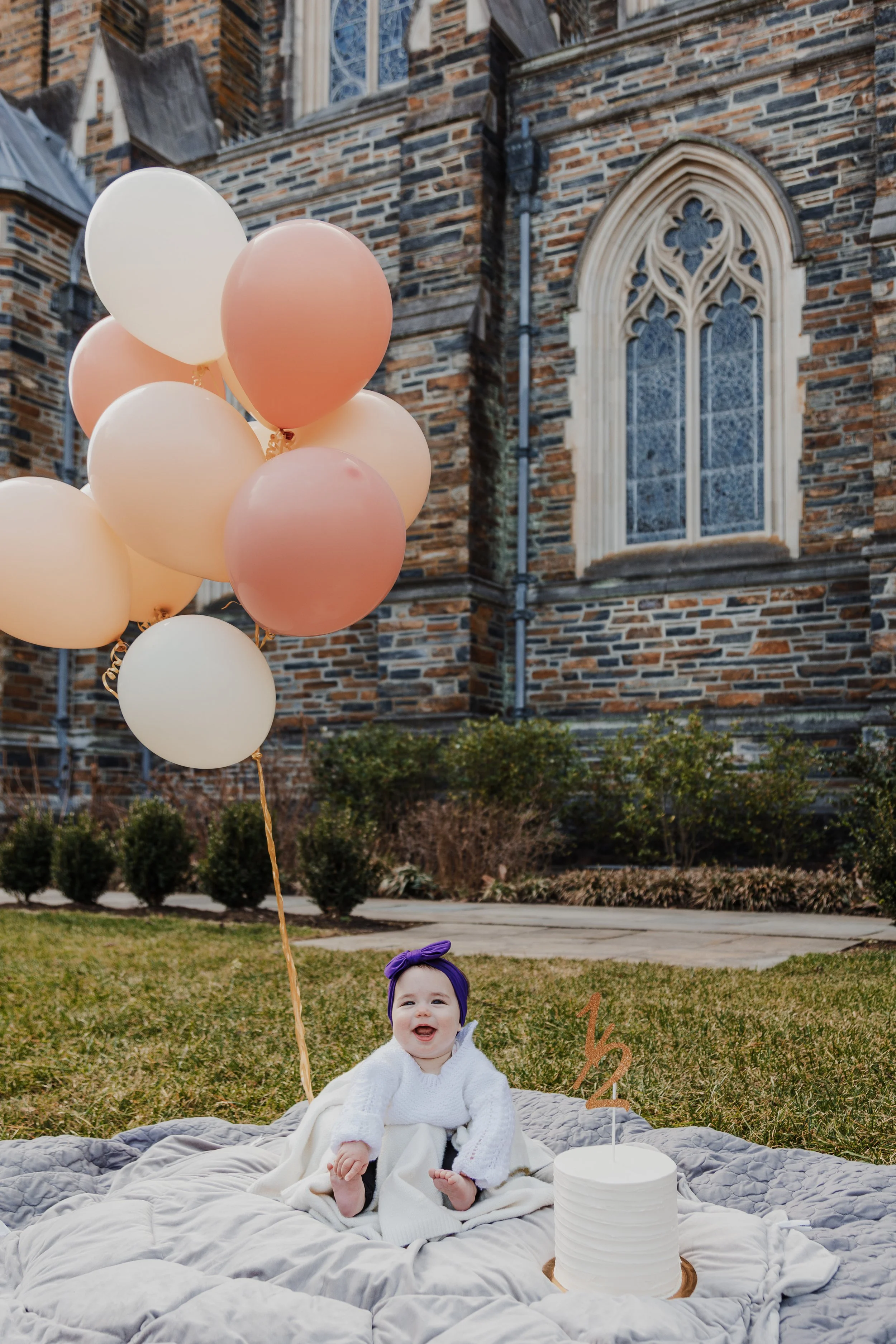 6-month-old baby sits next to cake and balloons in front of the Duke University Chapel in Durham, NC.