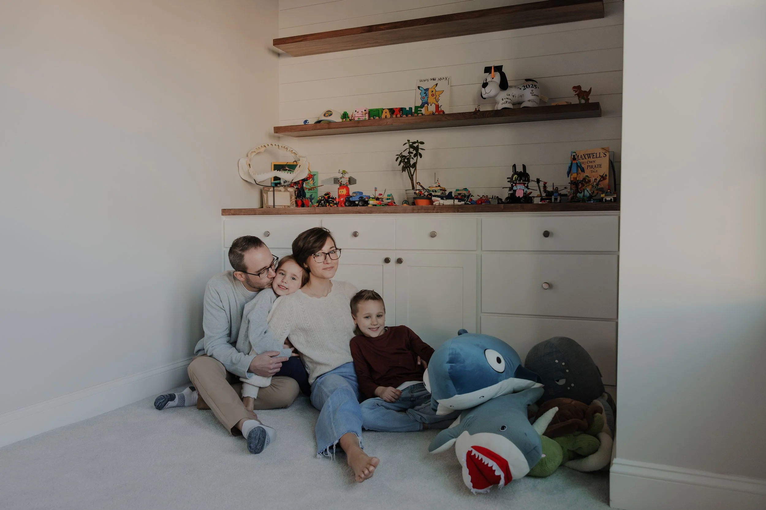 Family with 5-year-old and 7-year-old cuddle on the floor in front of a built-in bookshelf at their home in Wake Forest, NC.