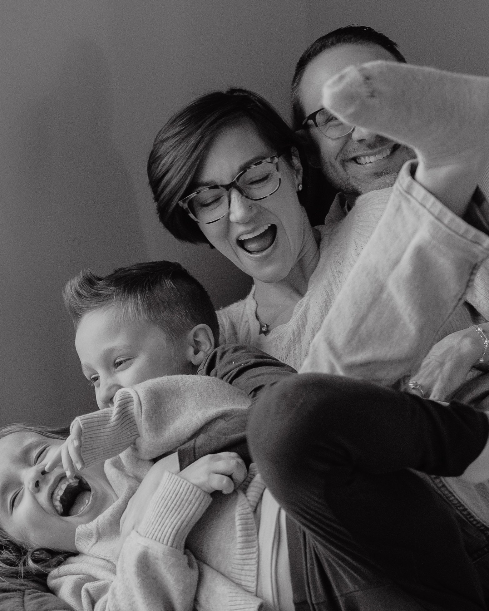 Black and white photo of a family tickling each other on a bed in their Wake Forest home.