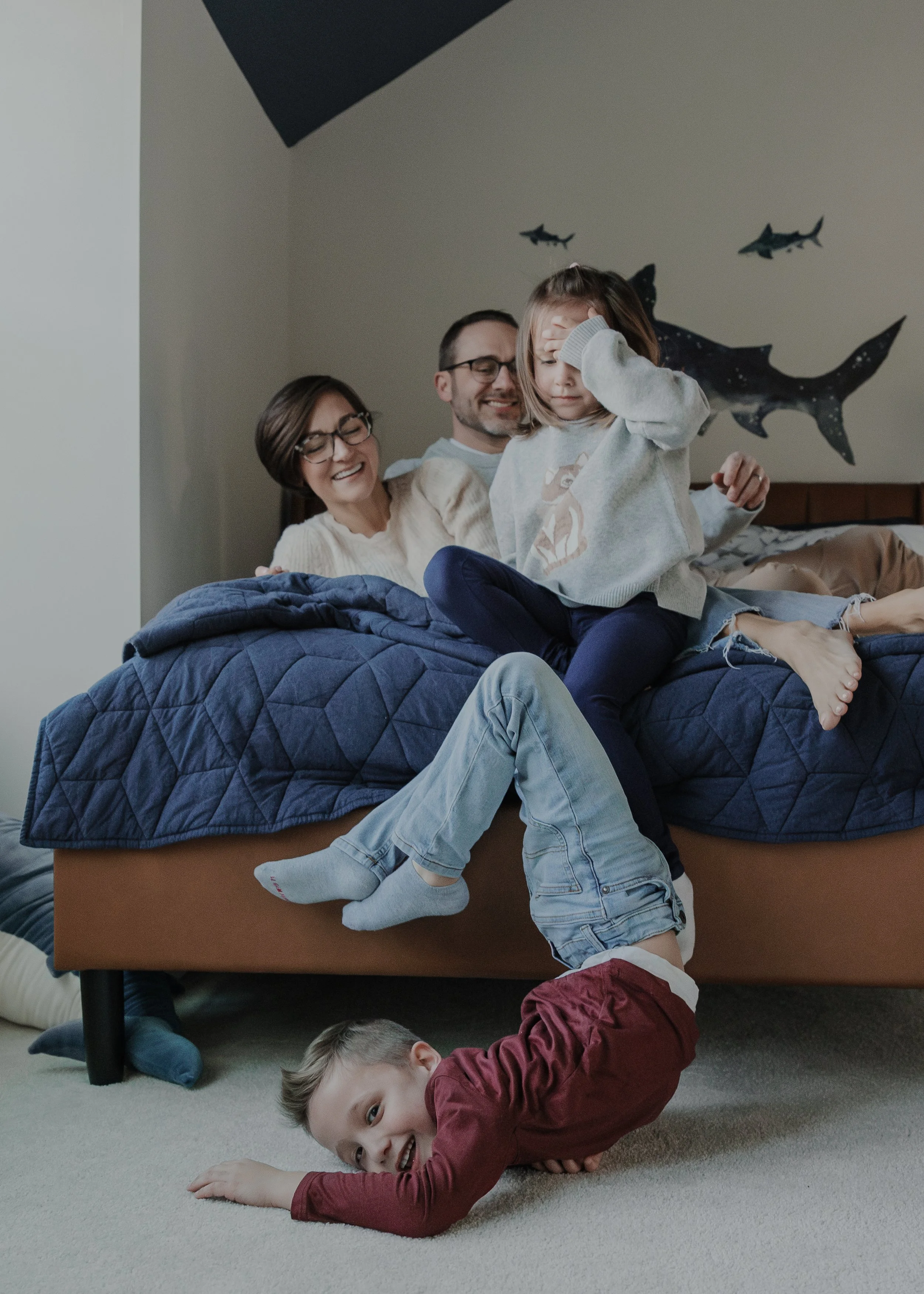 7-year-old boy tumbles on the ground while family watches from the bed during a family photo session captured at their home in Wake Forest, NC.