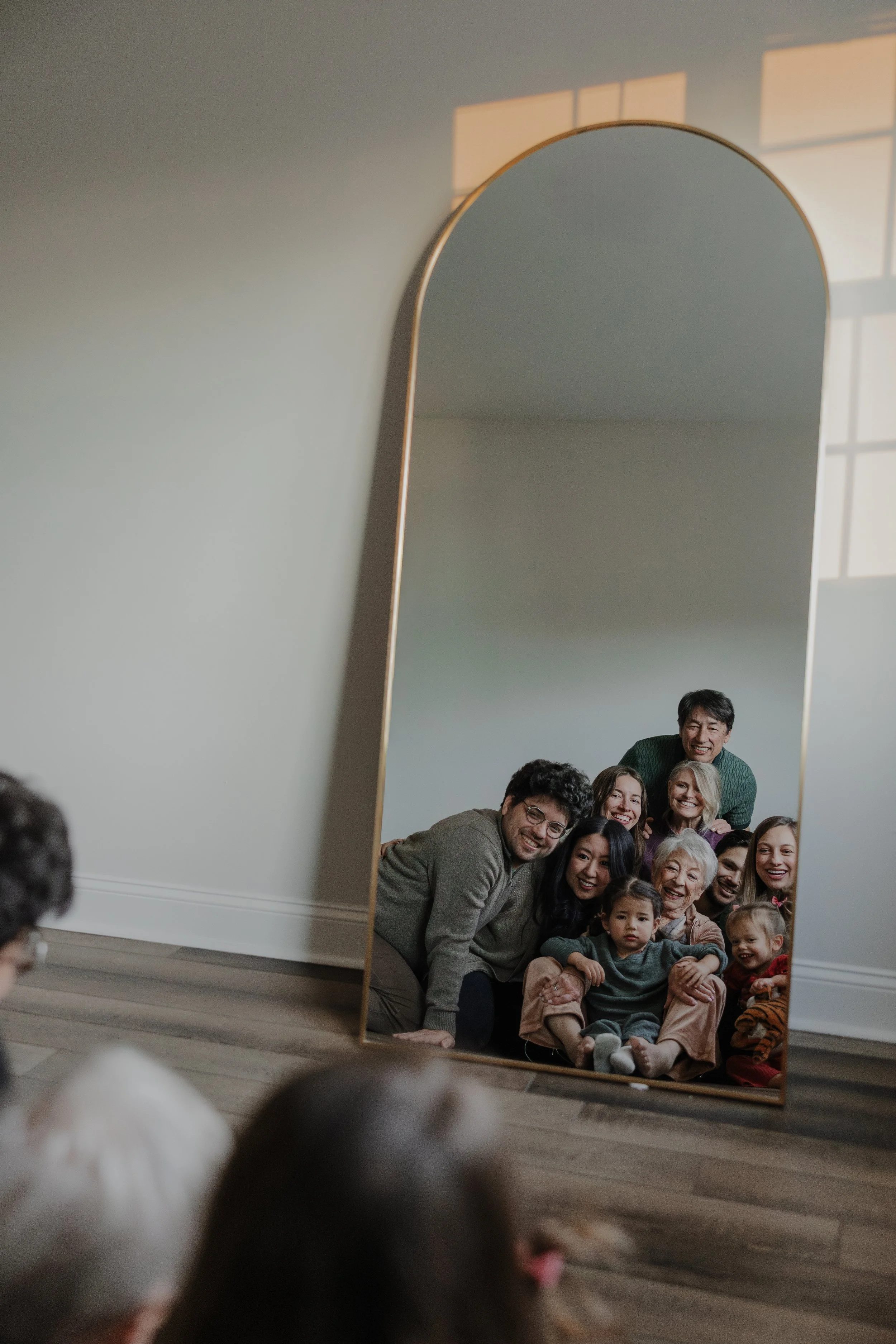 Extended family sits in front of a mirror and smiles at their reflections during an in-home family photo session in Chapel Hill, NC.