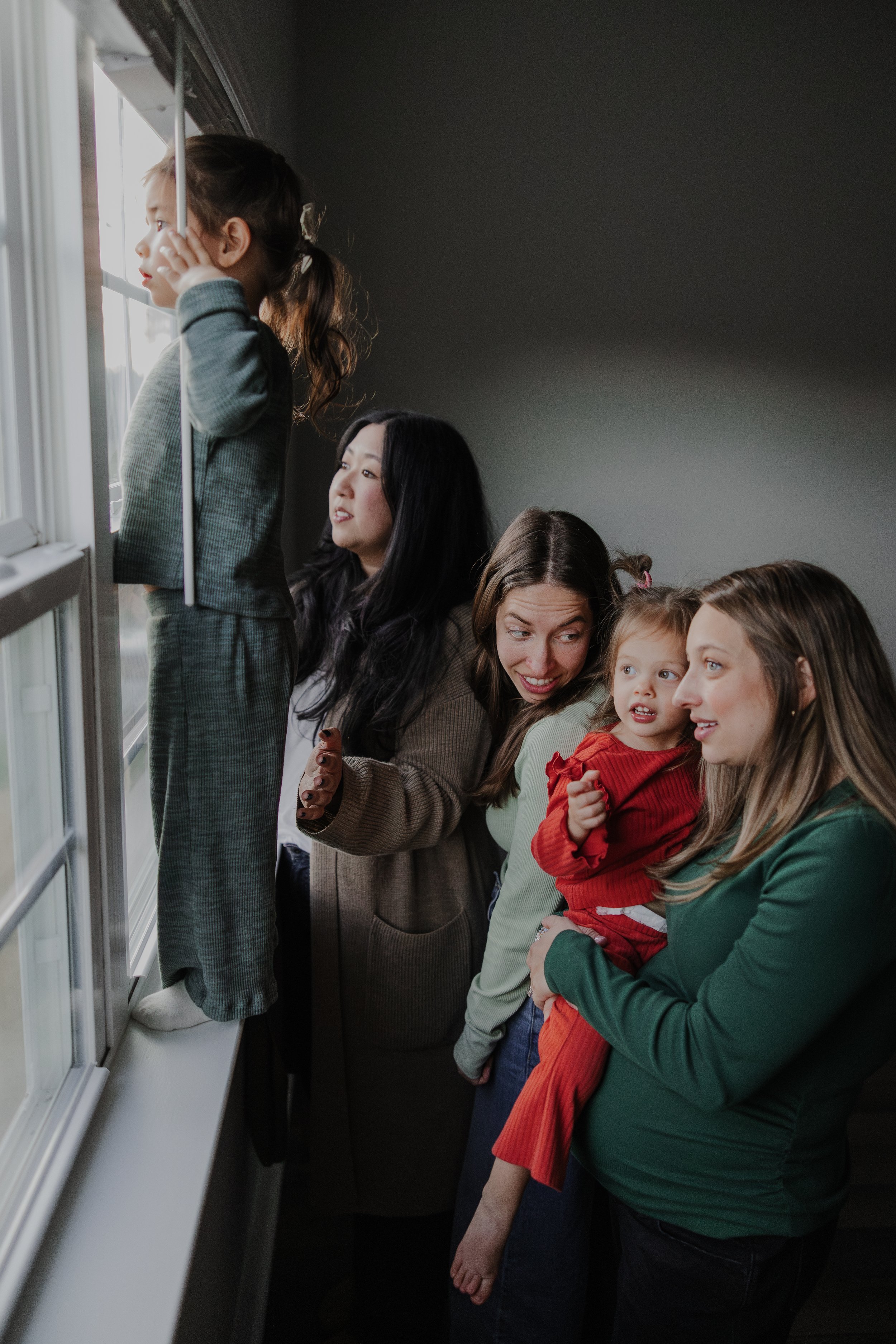 Family gathered by a window watching outside during an at-home photo session in Chapel Hill.