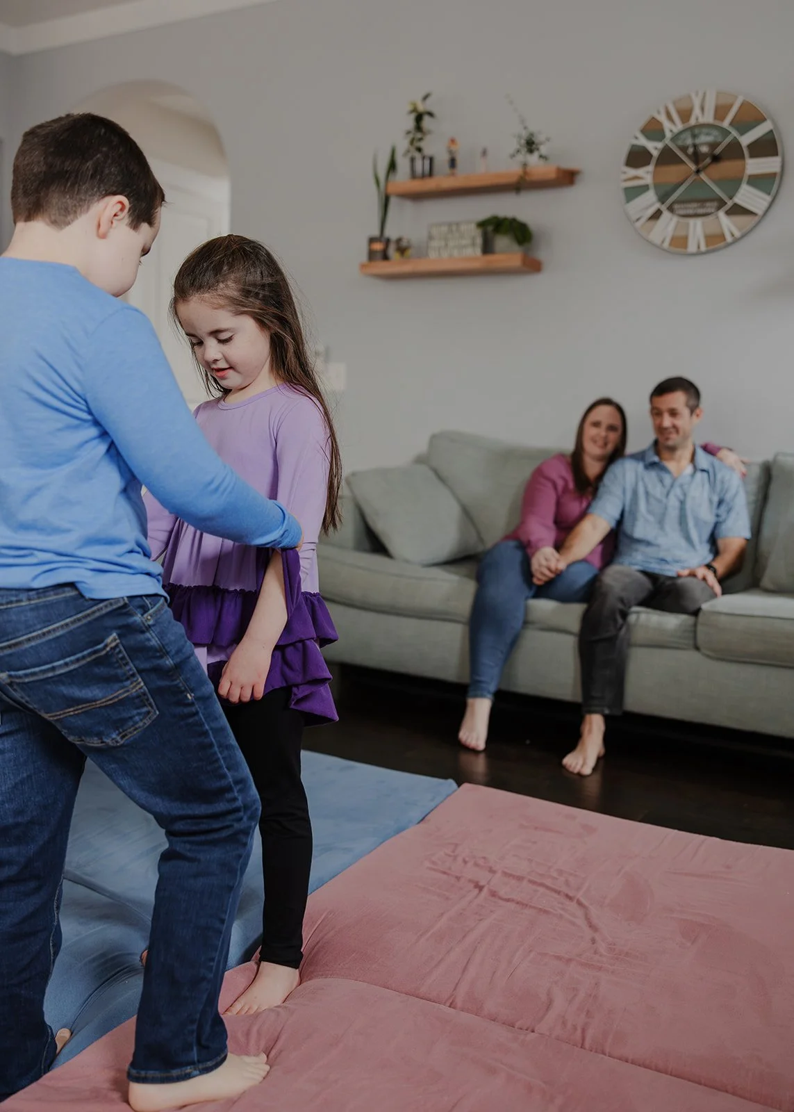 Children practicing jiu-jitsu together on floor mats while their parents watch from the couch during an in-home neurodivergent family photo session in Wake Forest, NC.