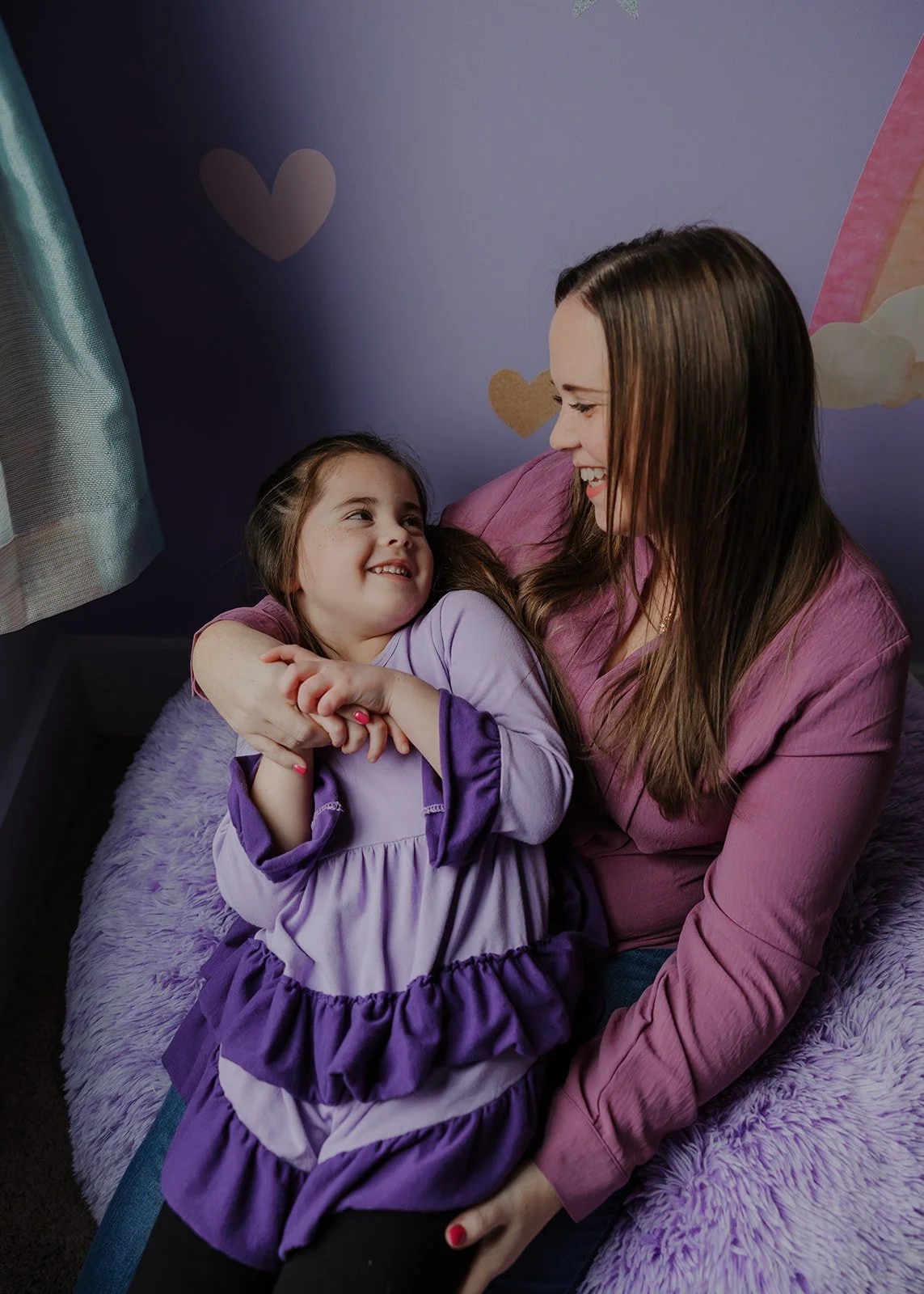 Mother cuddling her daughter in a purple bedroom during an in-home family photo session in Wake Forest, North Carolina.