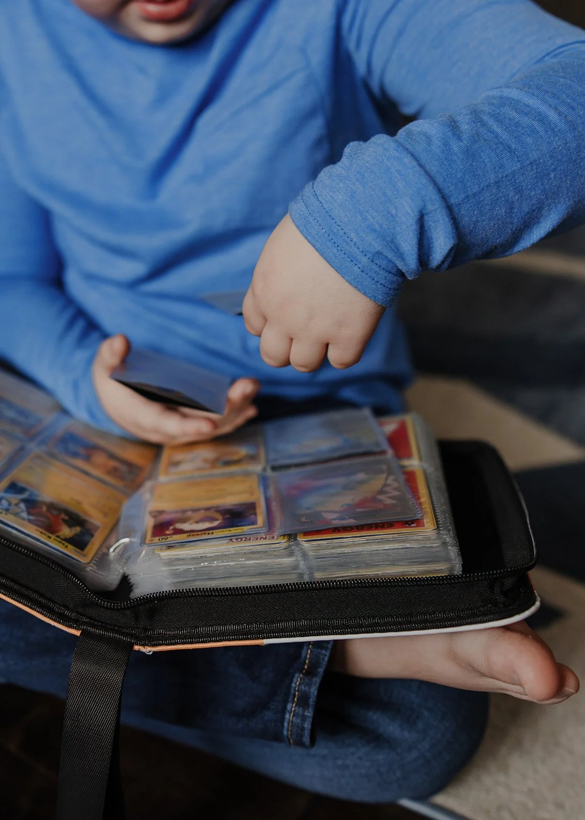 Child flipping through a binder of Pokémon trading cards during a relaxed in-home family photography session in Wake Forest, North Carolina.