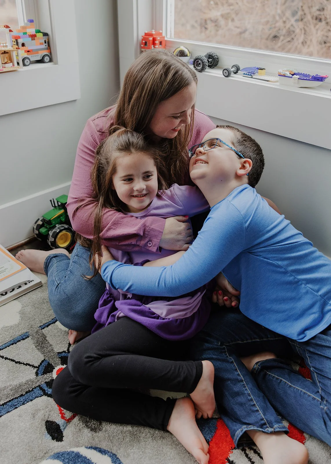 Mother sitting on the floor hugging her two children during an in-home family photo session in Wake Forest, NC.