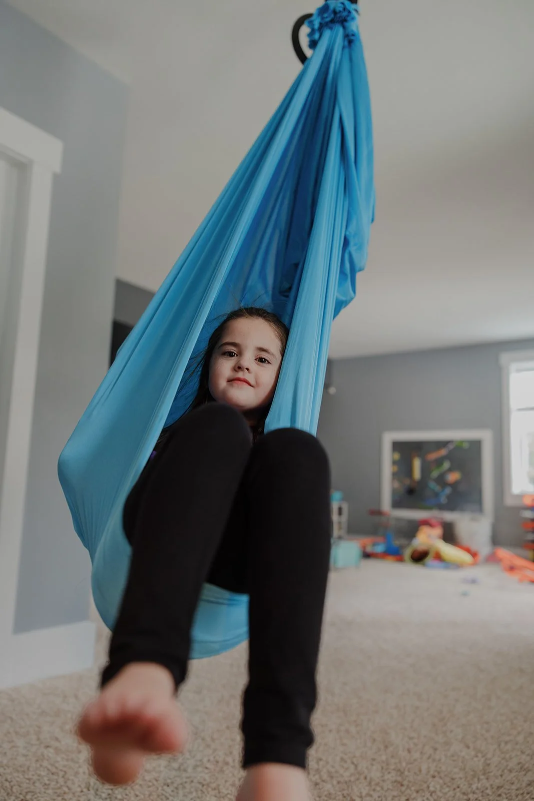 Child relaxing in a blue aerial sensory swing during an in-home family photo session in Wake Forest, NC.
