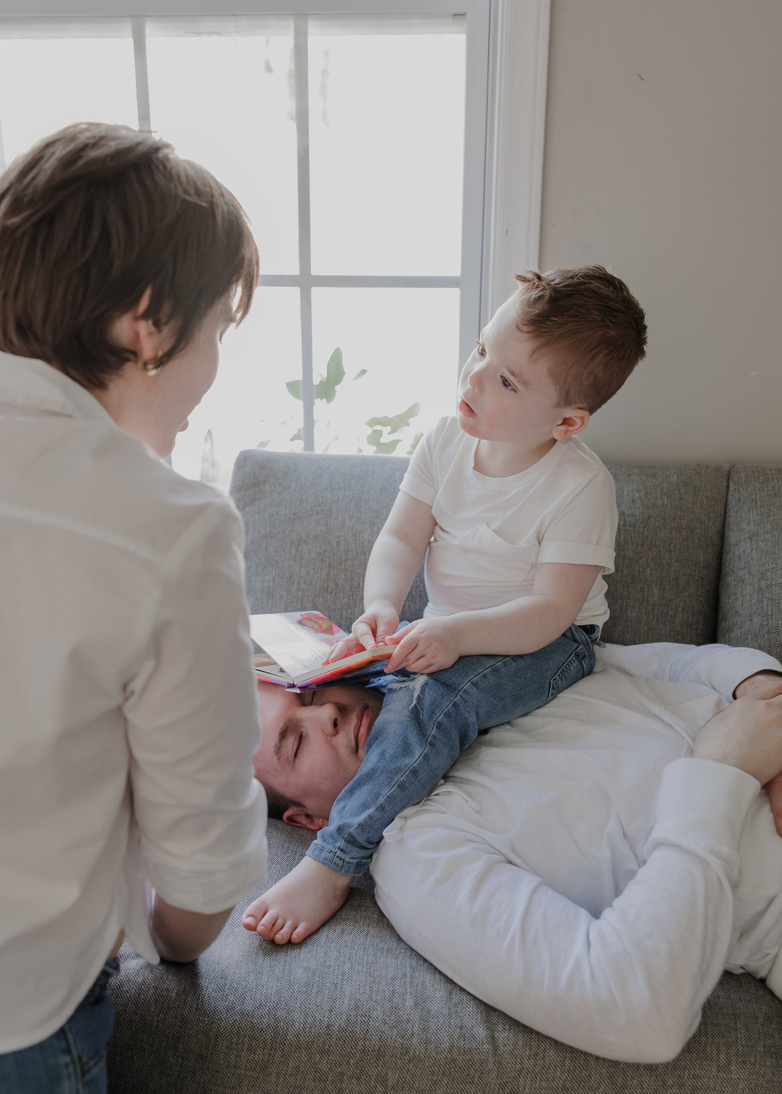Young boy sits on his father’s chest while holding a small book during a relaxed in-home family photography session in Durham, NC.