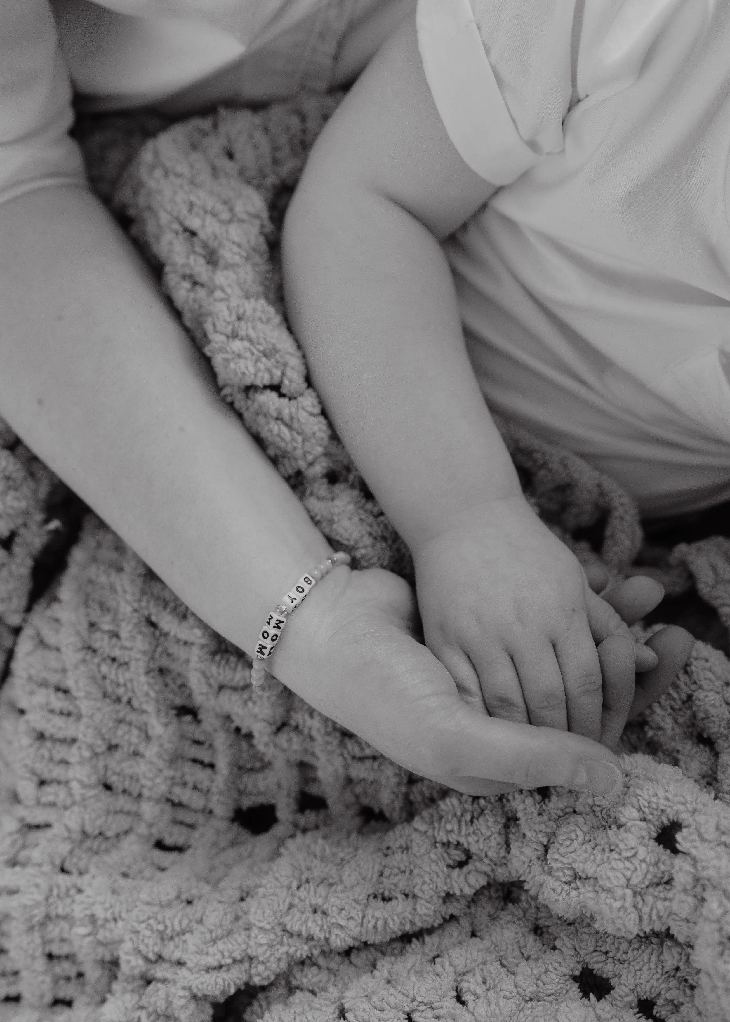 Close-up of a mother holding her child’s hand while wrapped in a soft blanket during an inclusive in-home family photography session in Durham, NC.