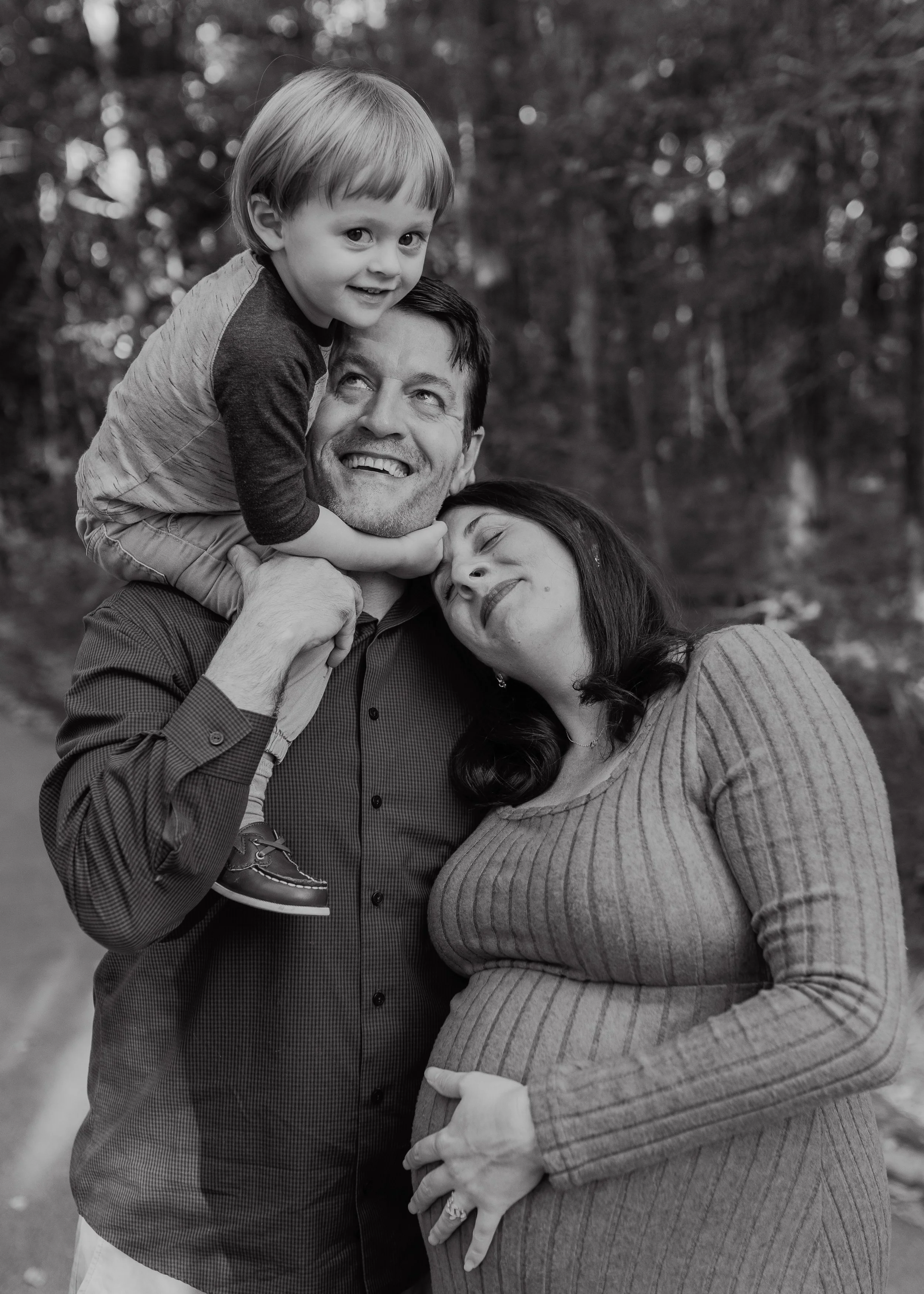 Black and white family photo of parents with their young child on dad’s shoulders, capturing a candid, connected moment during a Raleigh outdoor family session
