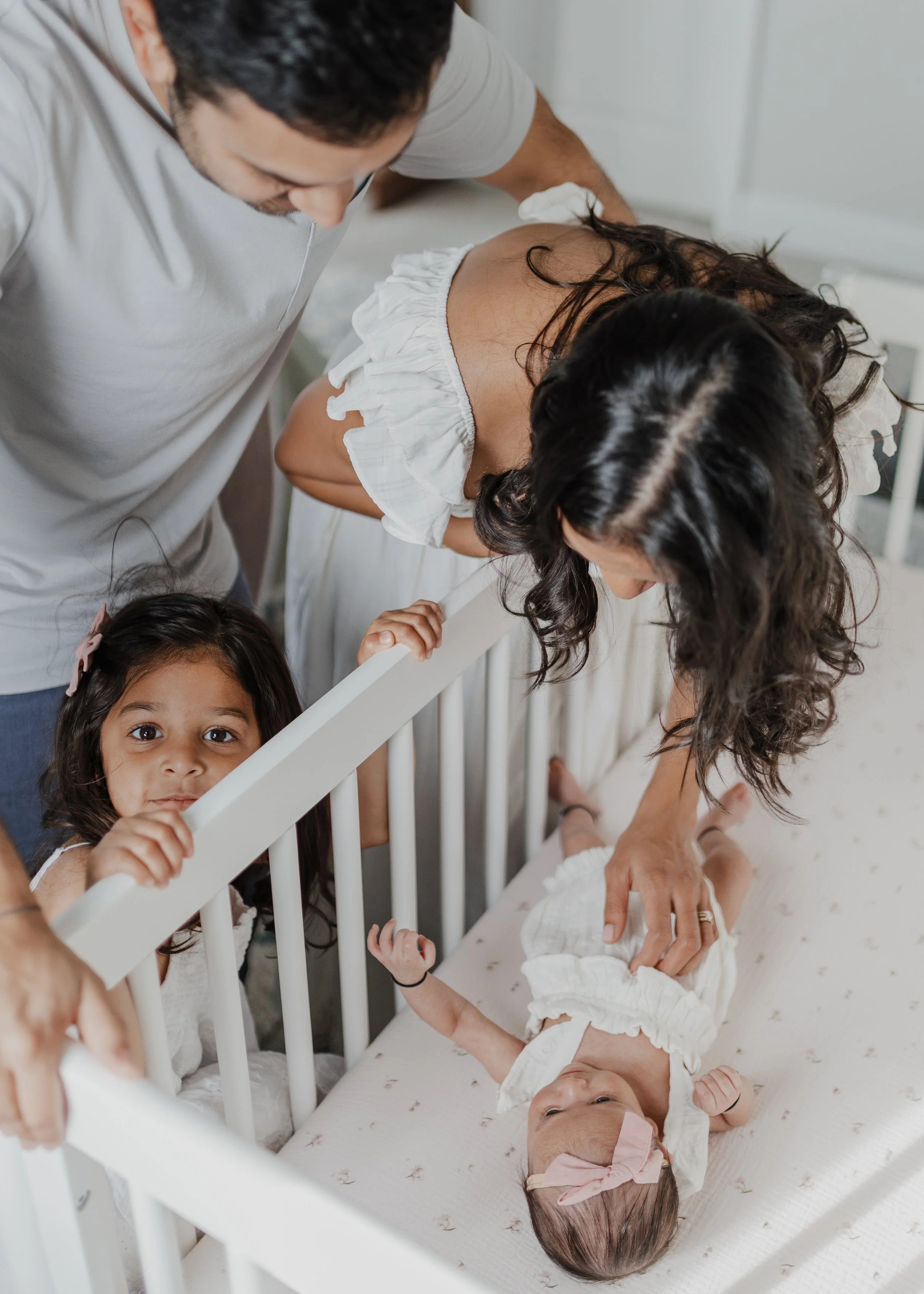 Parents and young sibling gathered around newborn baby in crib during a natural in-home newborn photography session in Raleigh