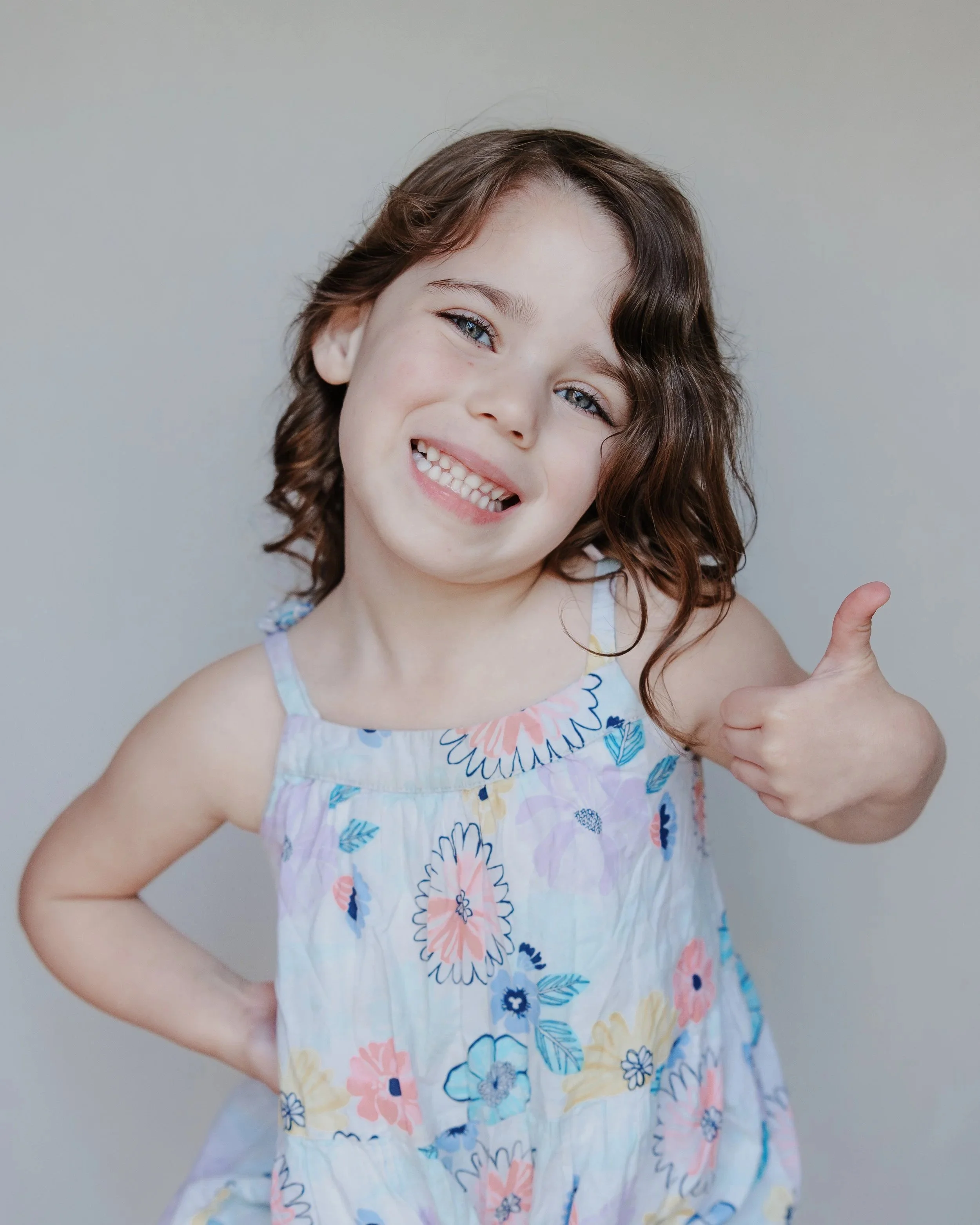 A young girl with curly brown hair giving a thumbs up and smiling during a boutique school photography session in Raleigh.