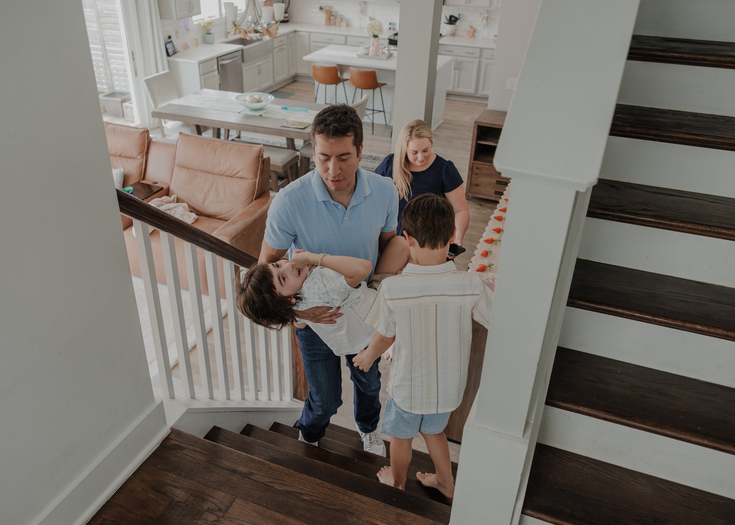A high-angle shot of a father carrying his special needs son up the stairs while his other children follow during a Wendell home session.