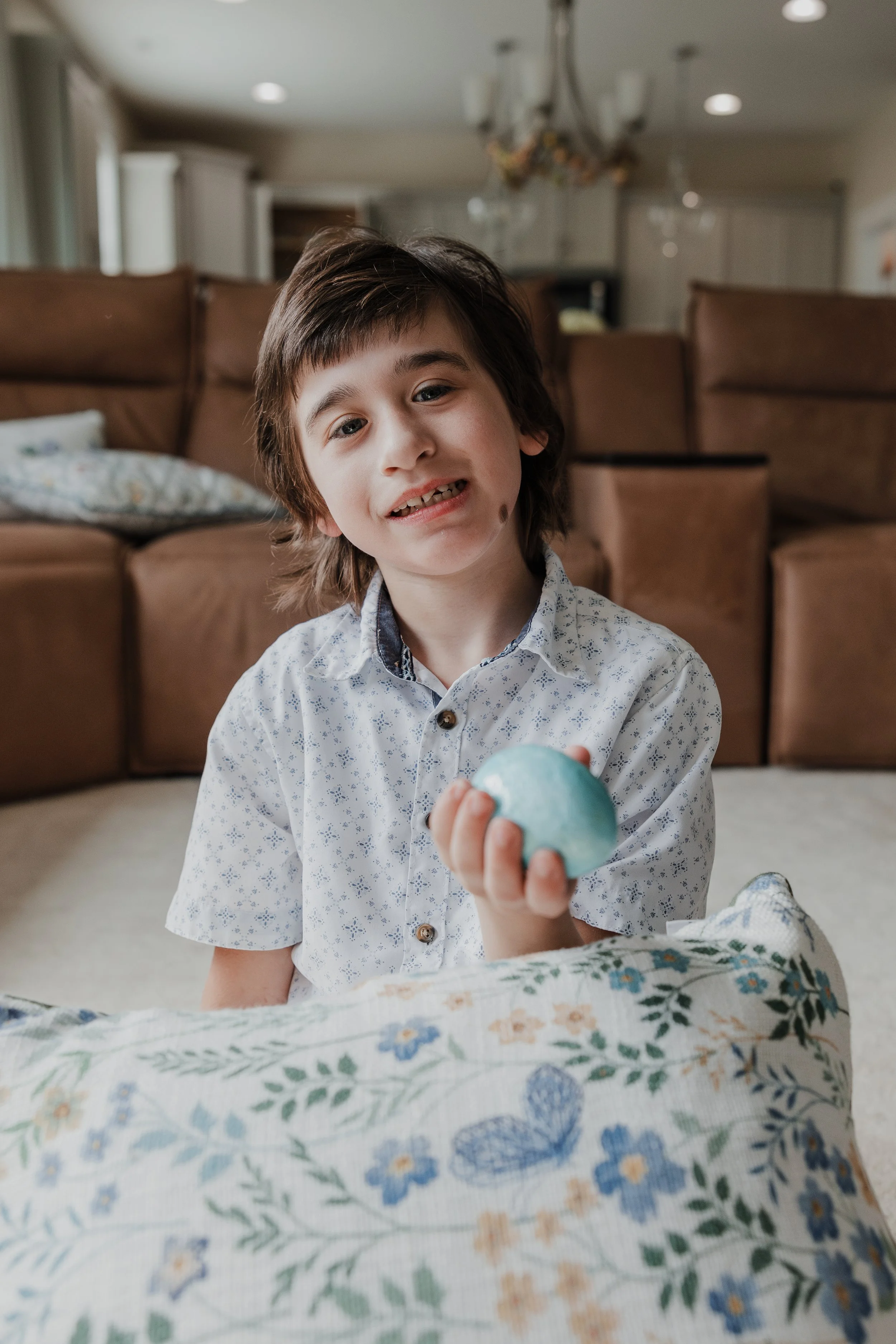 A candid portrait of a young boy holding a blue egg during a special needs family photo session in Wendell, NC.