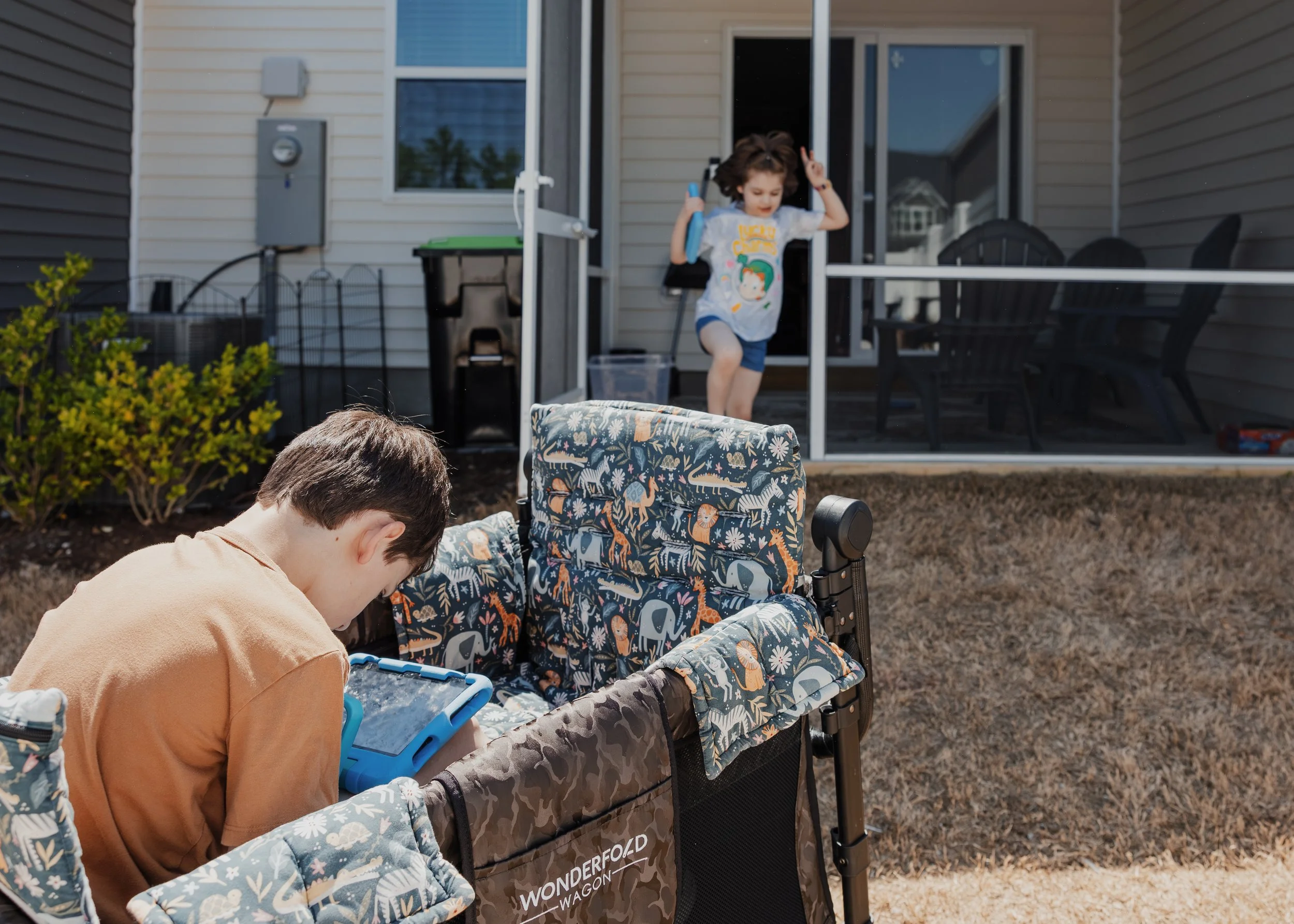 A profoundly autistic boy sits in a WonderFold wagon while his sister runs out of their Wake Forest home before a family photo session.