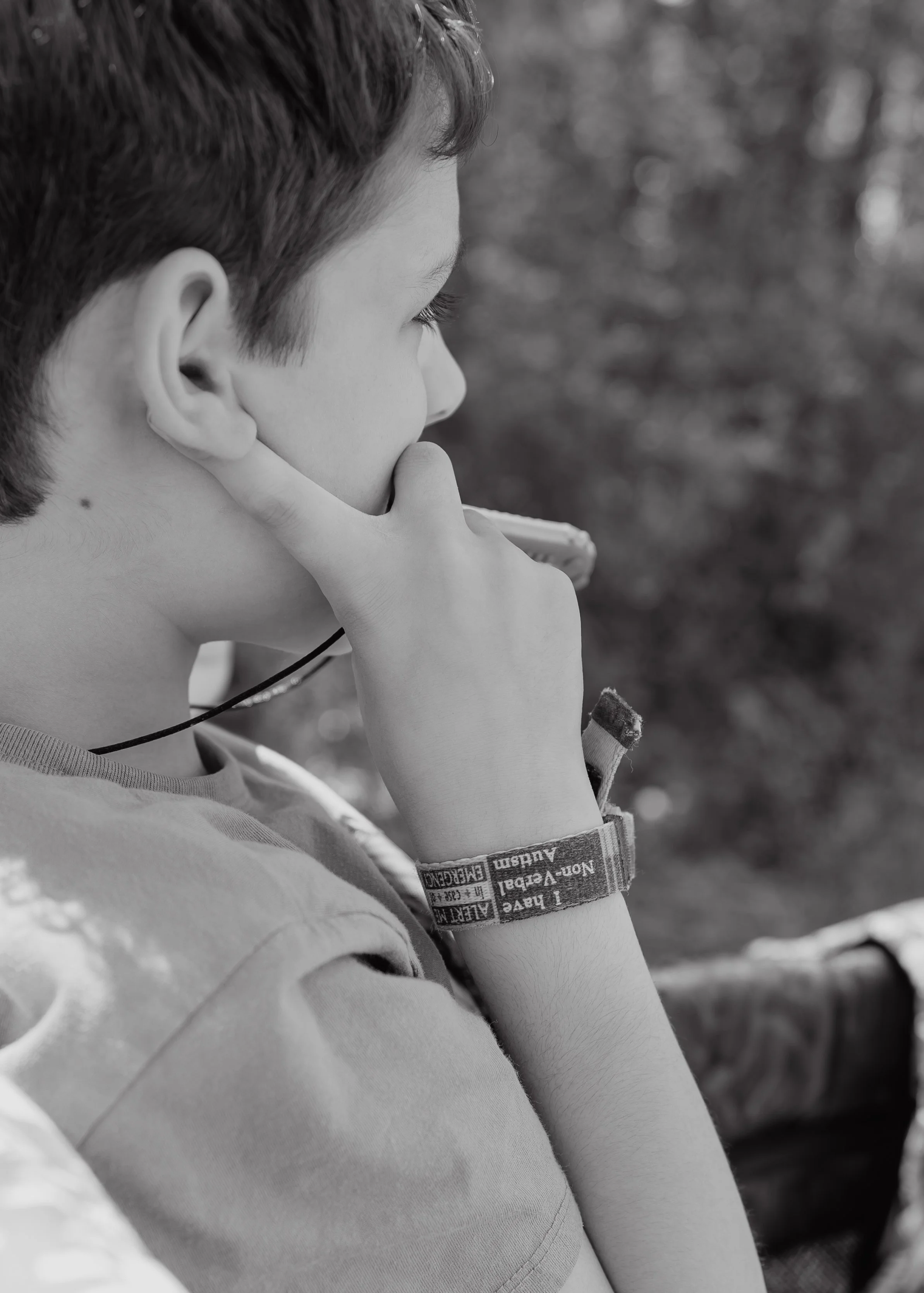 Black-and-white portrait of a profoundly autistic, largely nonverbal boy sitting quietly in a WonderFold wagon during a family photo session in Wake Forest.