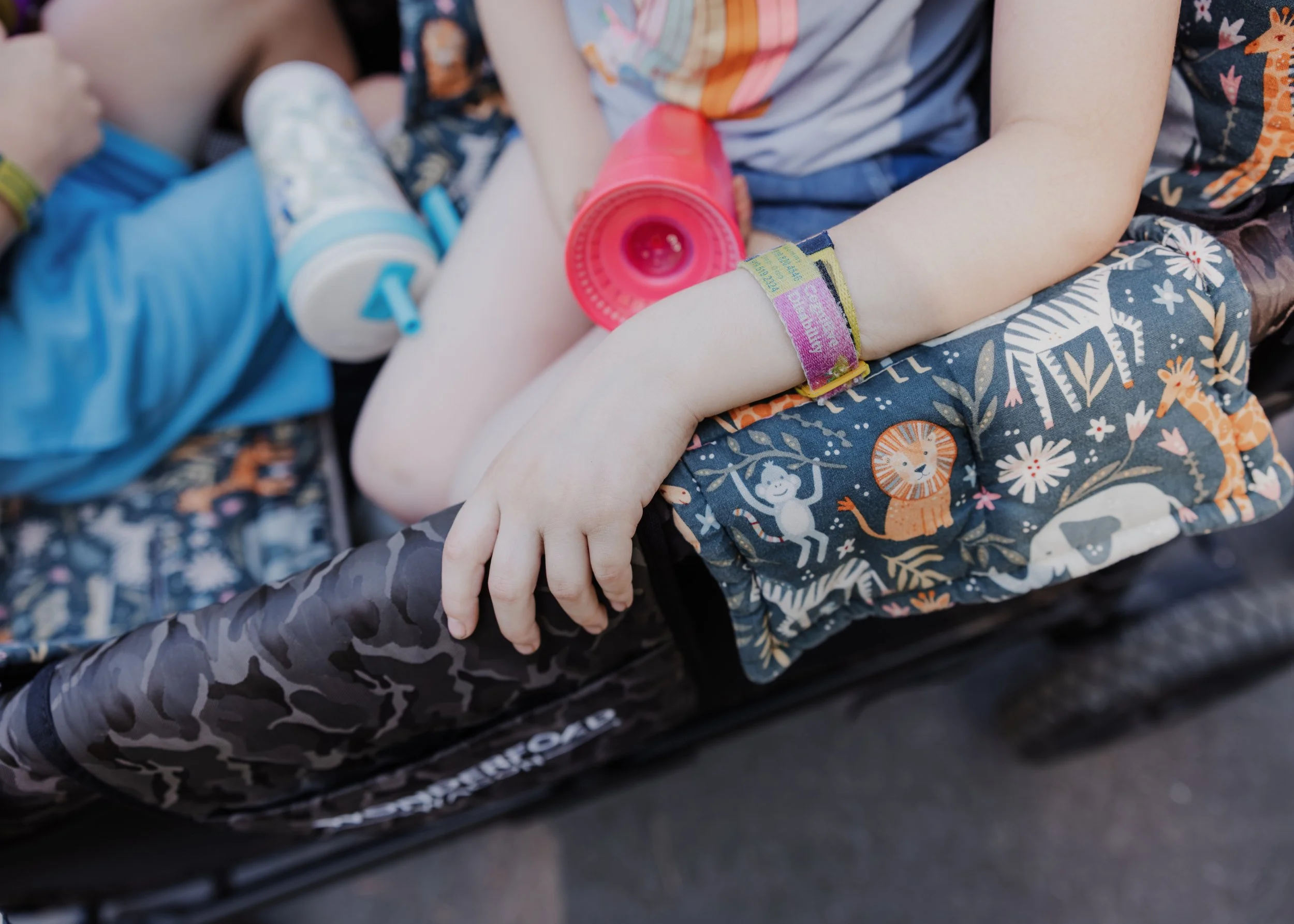 Close-up of two children's autism awareness safety bracelets and comfort items resting on a WonderFold wagon during a family photo session in Wake Forest.