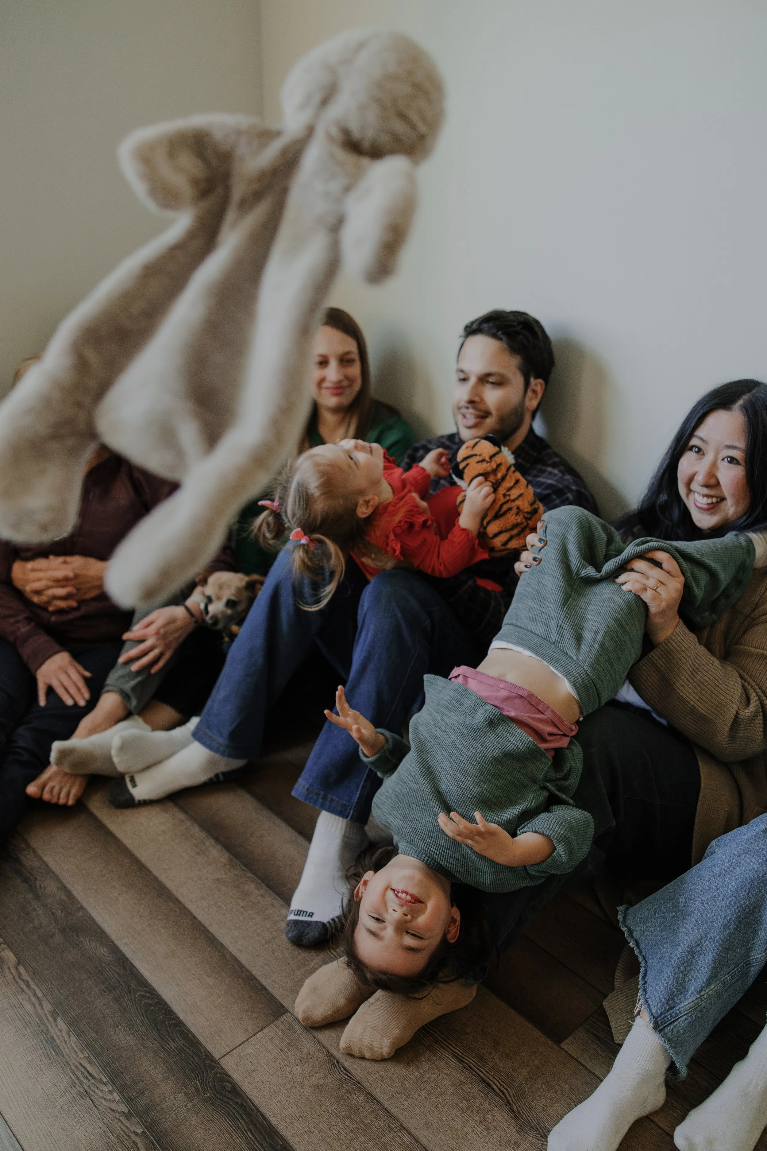 4 generations of family members sit on the floor and play with toddlers during a generational family session in Chapel Hill, NC.