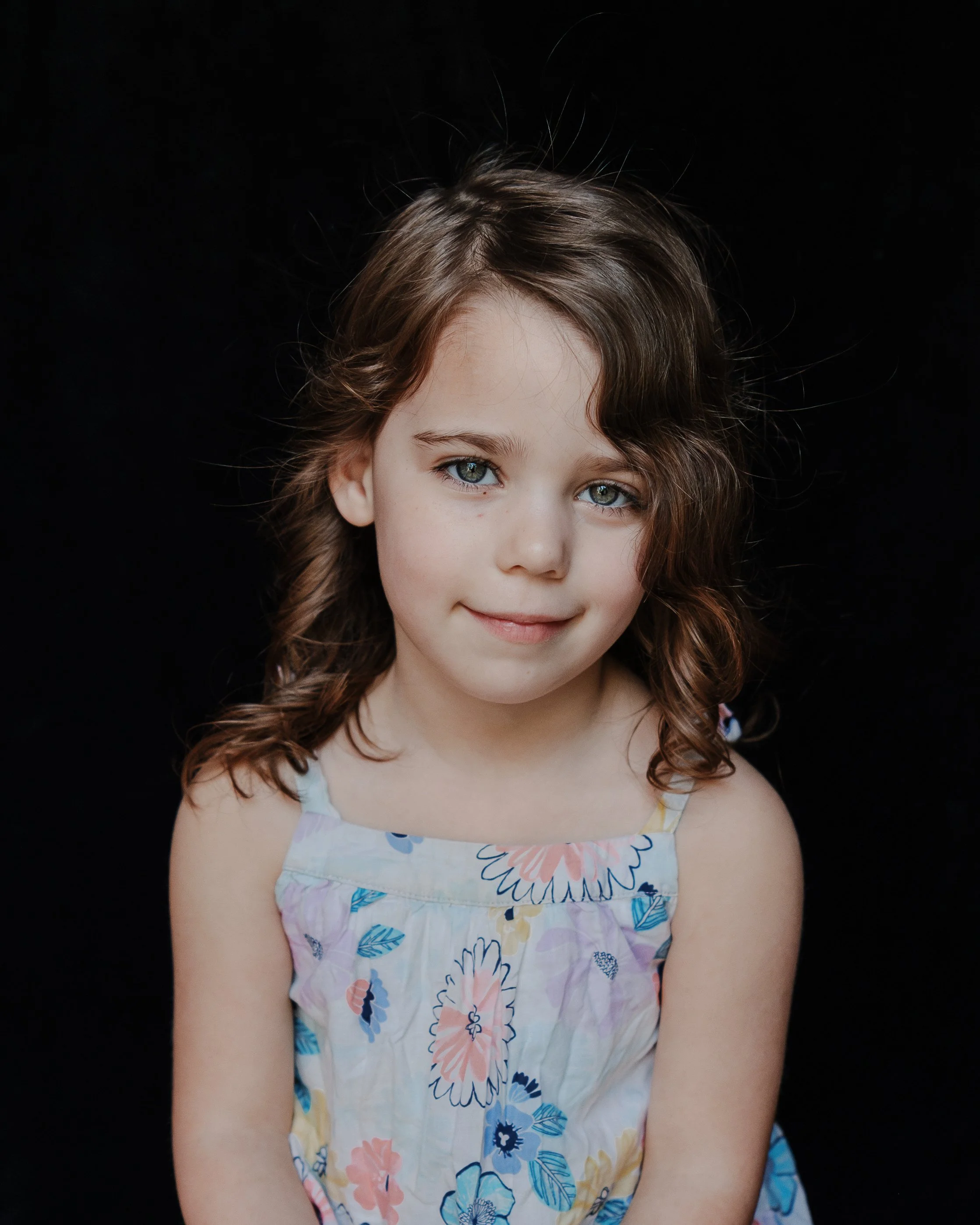 A cinematic, fine art school portrait of a young girl with curly hair against a dark backdrop, showcasing an authentic and soulful expression.