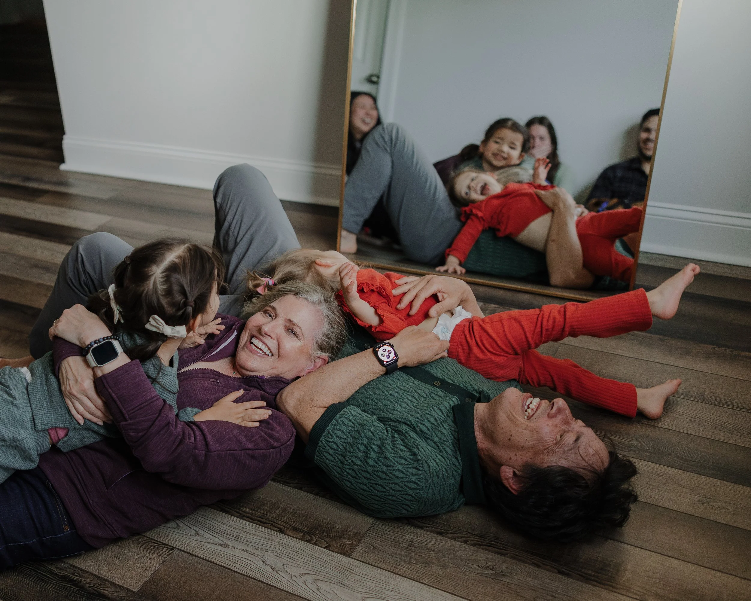 Four generations laughing together on the floor during an at-home extended family photo session in Chapel Hill.