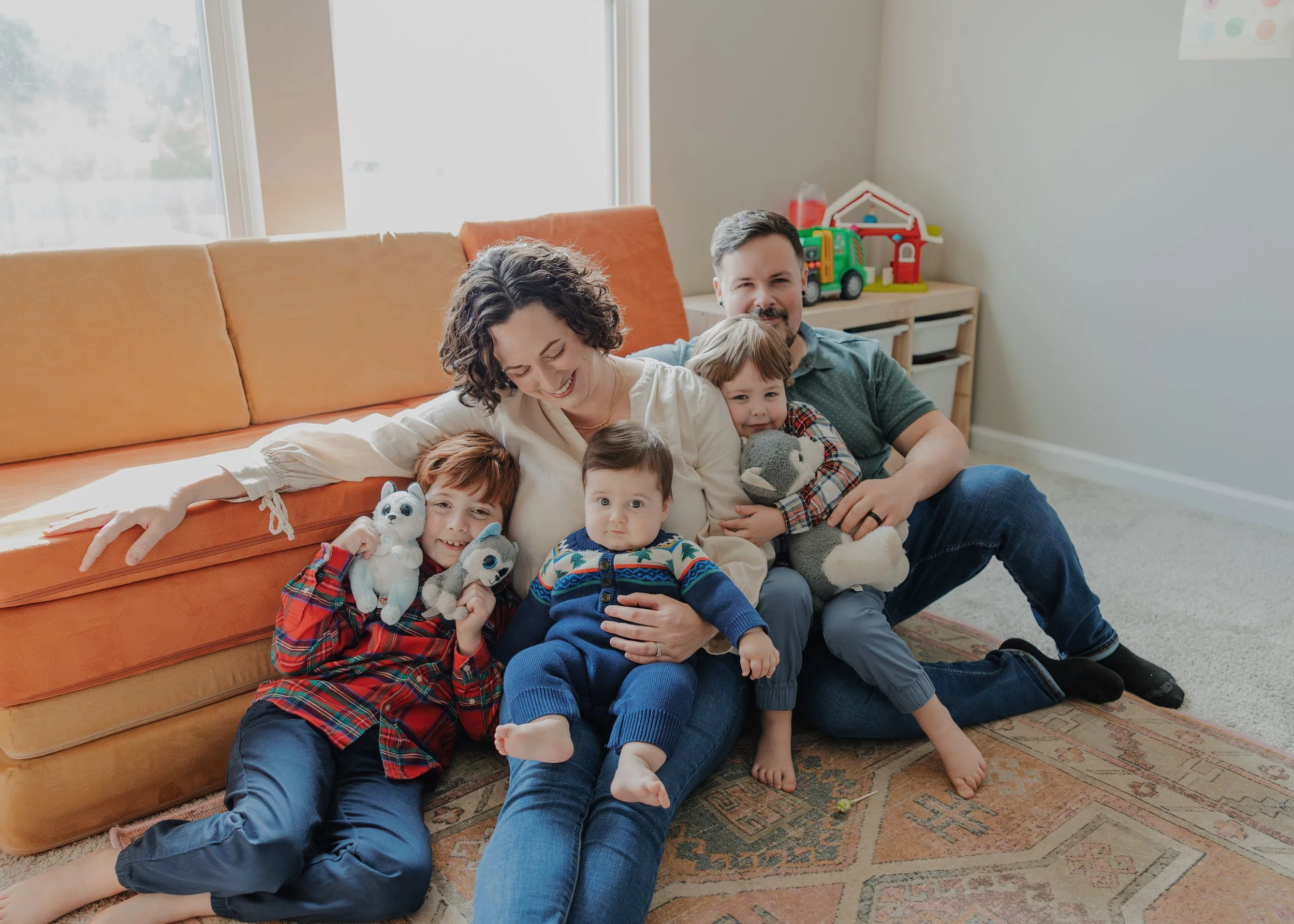 Family with three kids sits in front of nugget couch and plays with stuffed animals during a family photo session at their home in Raleigh, NC.