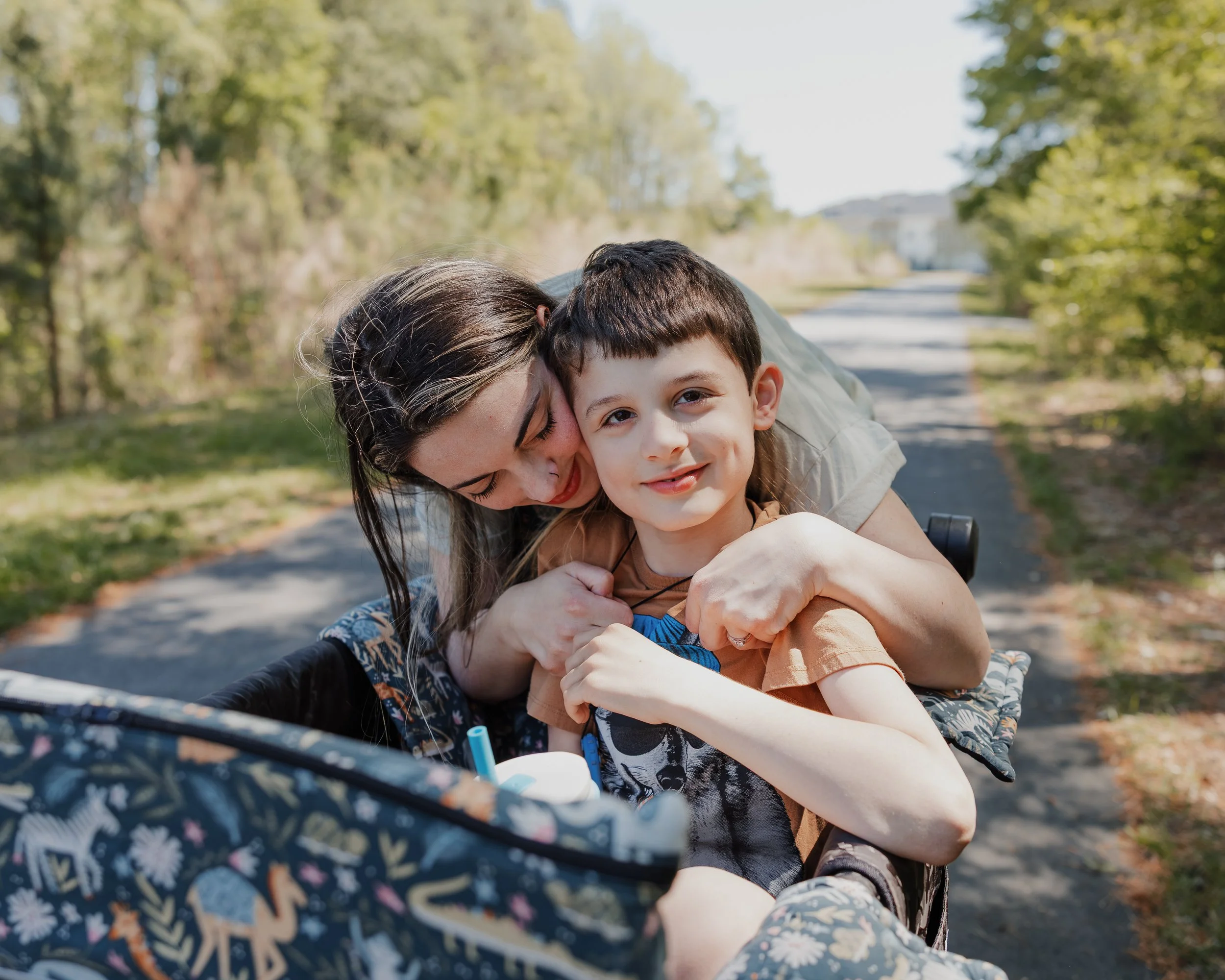 A mother hugs her profoundly autistic son as he sits in a WonderFold wagon on a Wake Forest greenway during an autism-friendly family photo session.
