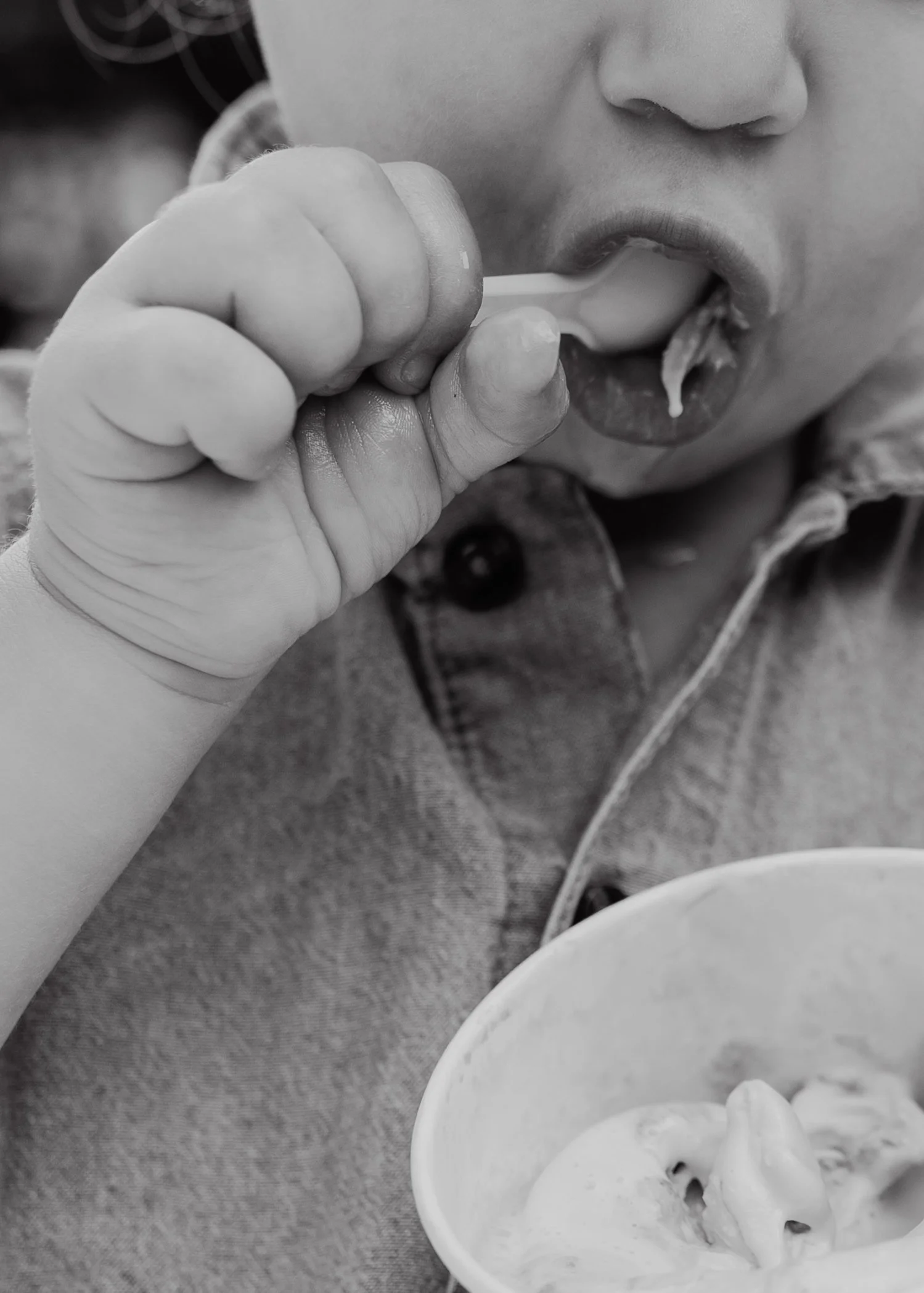 Black-and-white close-up of a toddler eating ice cream with a spoon