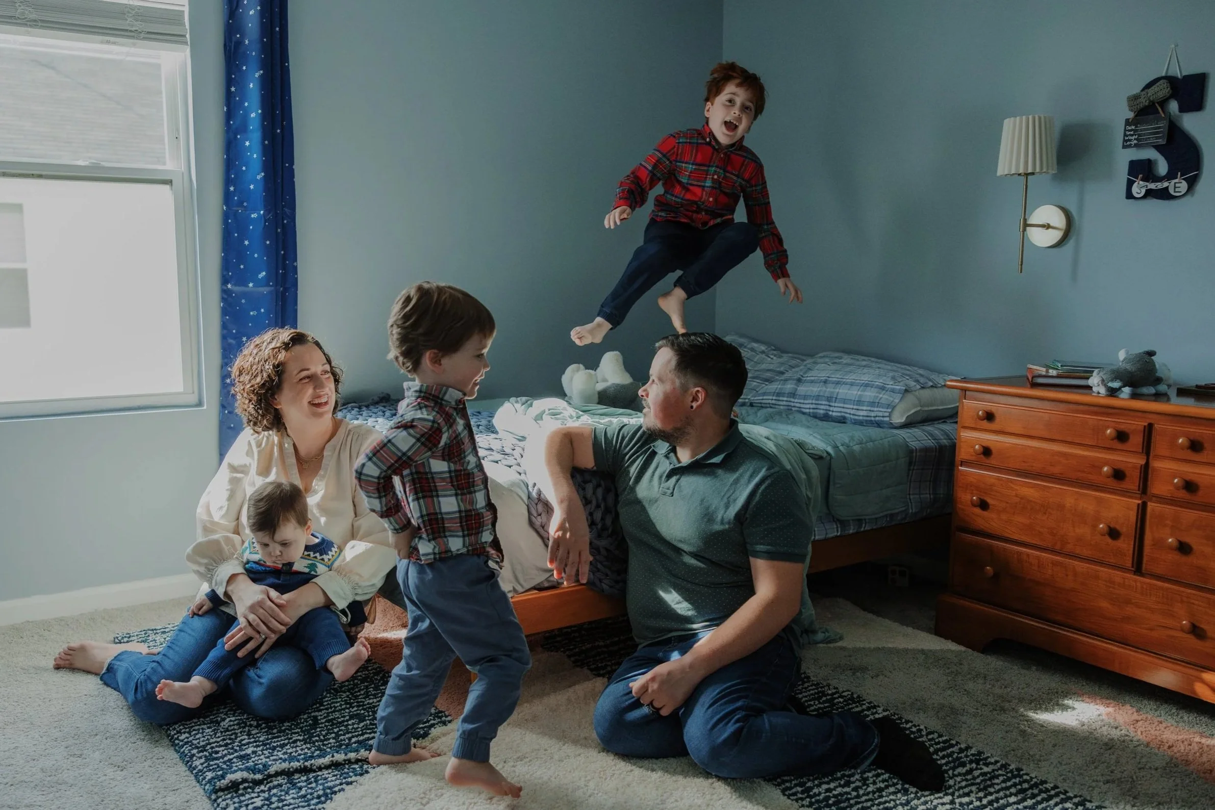 Family with 3 young boys play in a bedroom during an in-home lifestyle family photo session in Raleigh, NC.