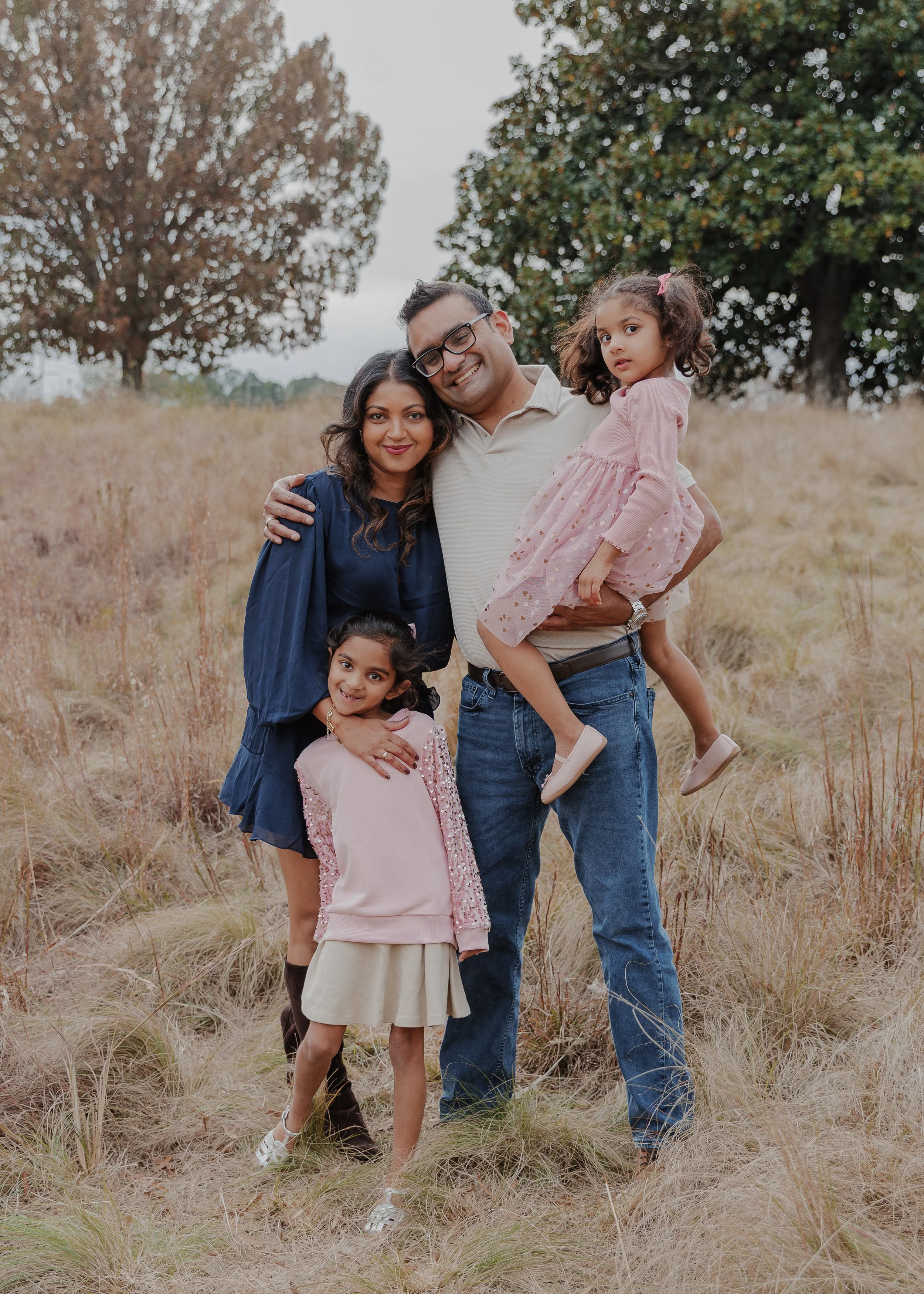 A family of four shares a playful moment during a Raleigh fall mini session at NCMA Park, with two sisters riding on their parents' shoulders.