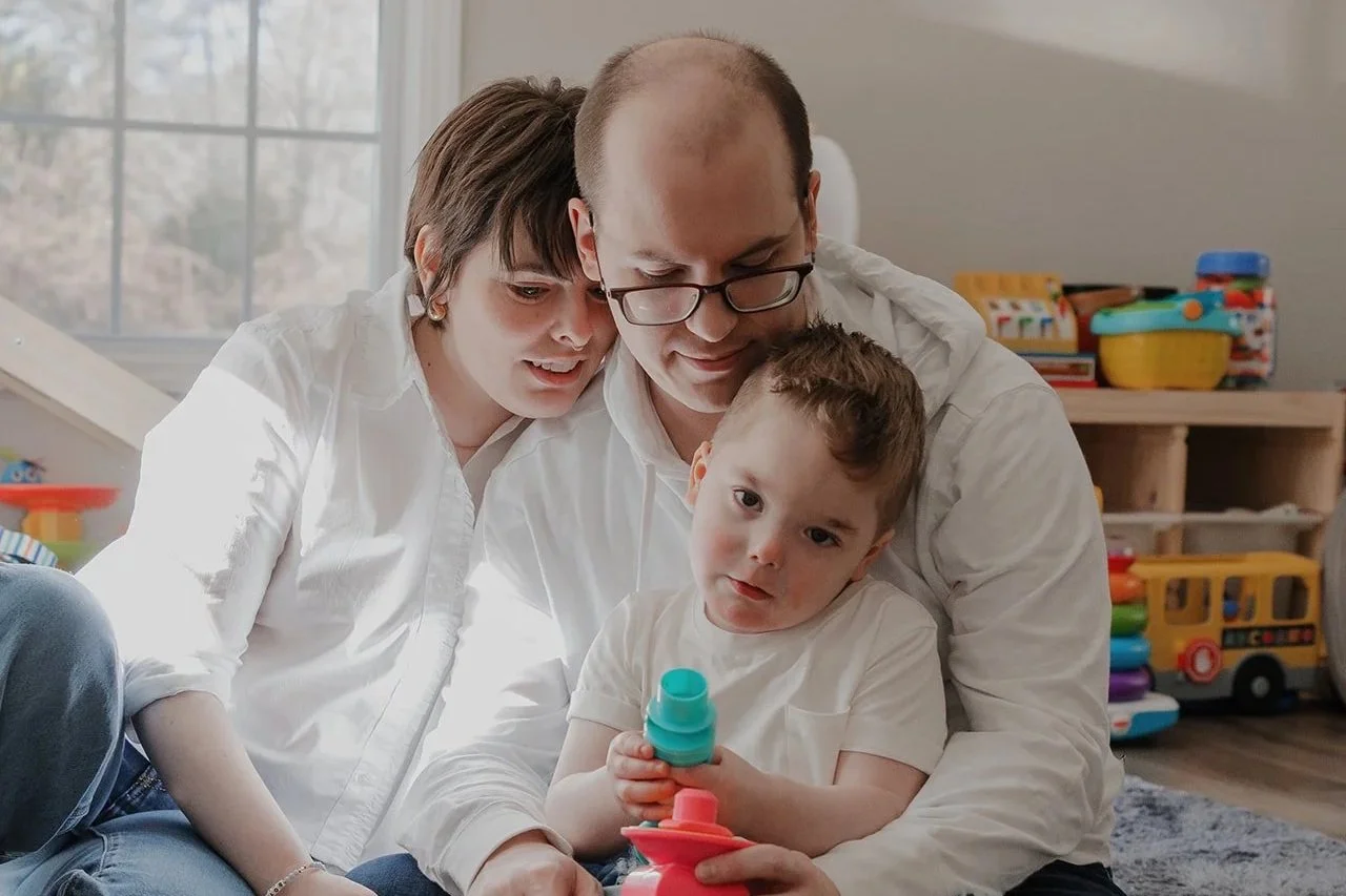 Parents sit on the floor with their young son playing with stacking toys during an inclusive in-home family photography session in Durham, NC for a child with ADNP Syndrome.