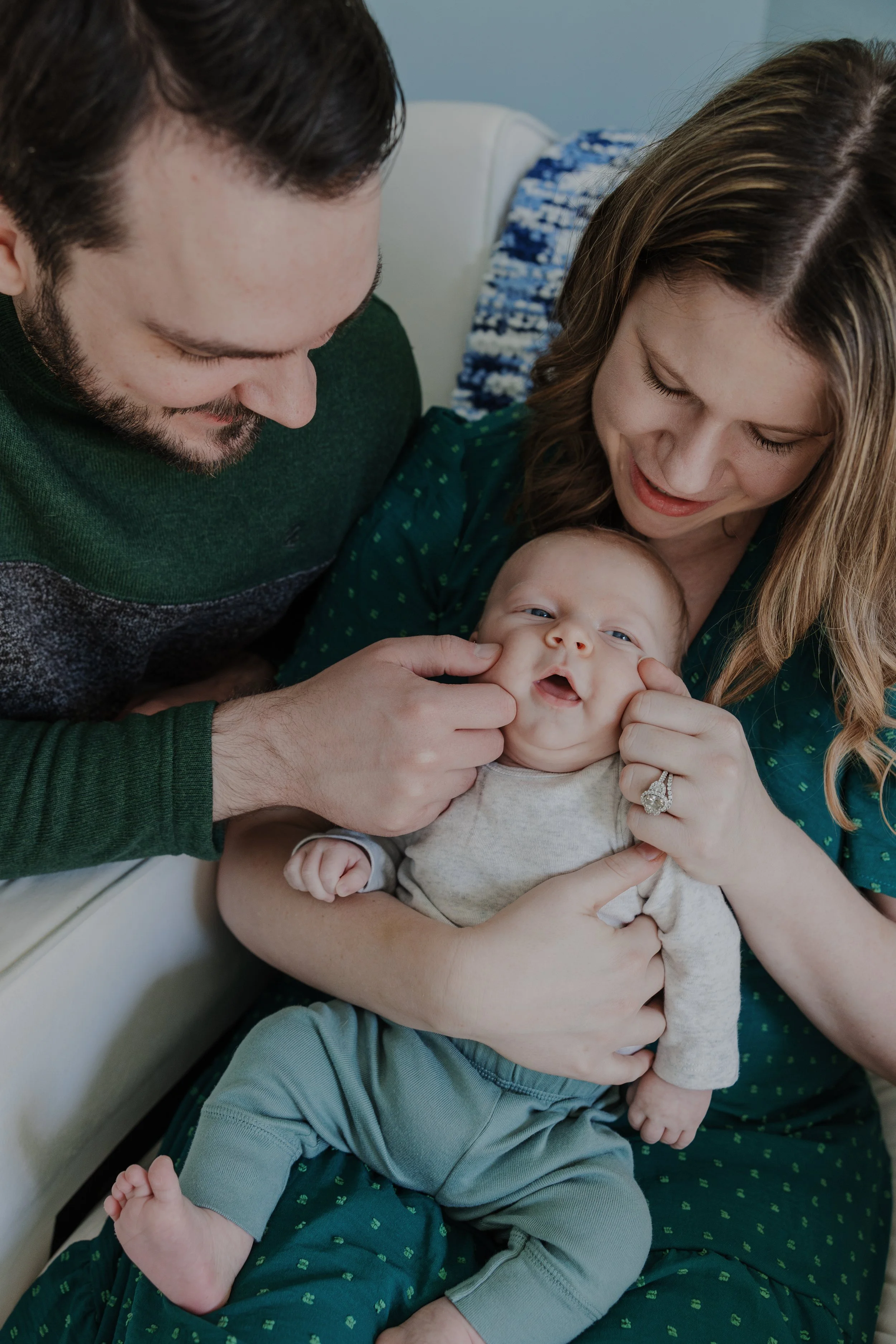 Parents smiling and gently holding their newborn baby during a cozy in-home newborn photography session in Raleigh