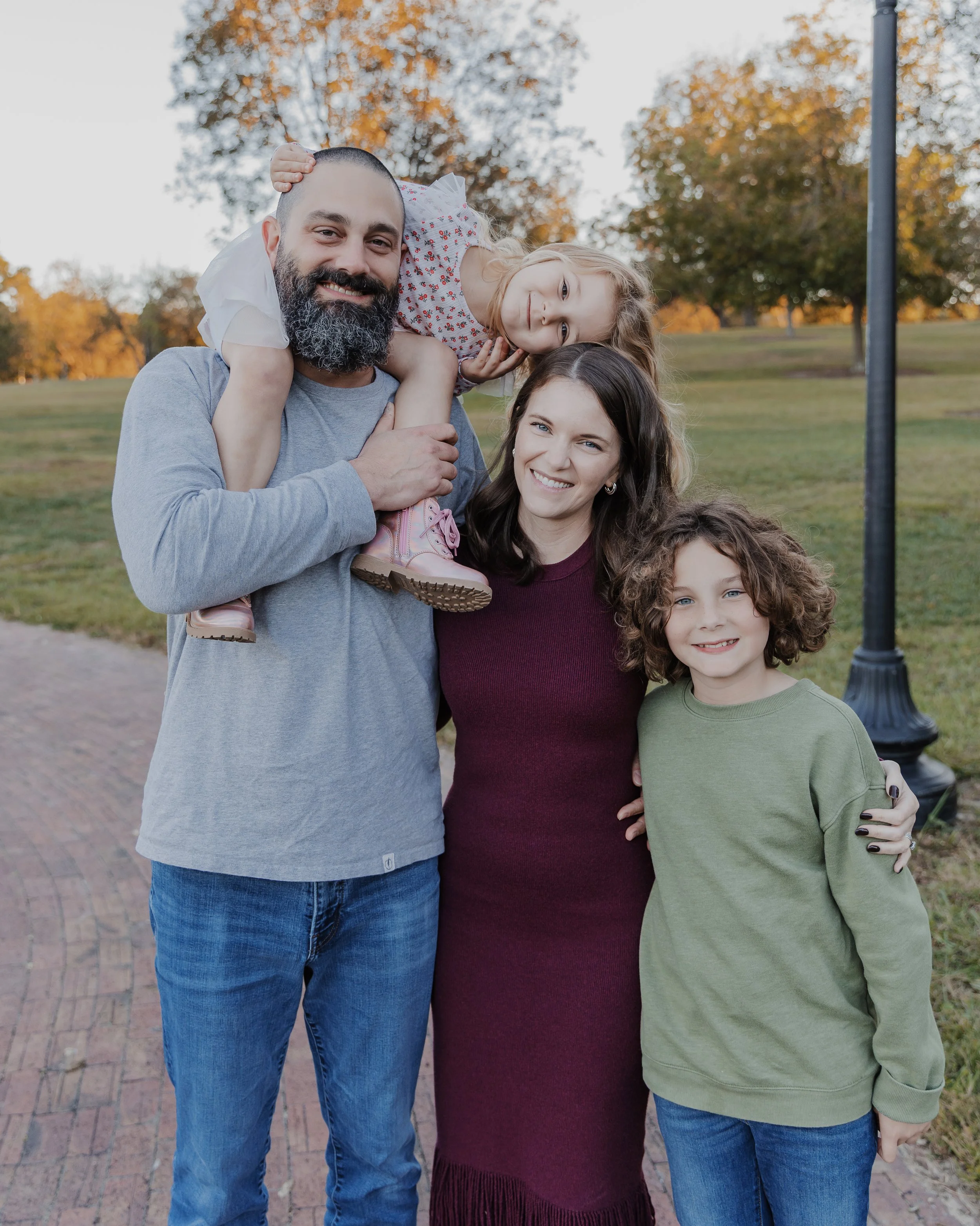 Father holding his daughter on his shoulders as their family of four smiles together during a fall family photo session at Historic Oak View County Park in Raleigh, NC.