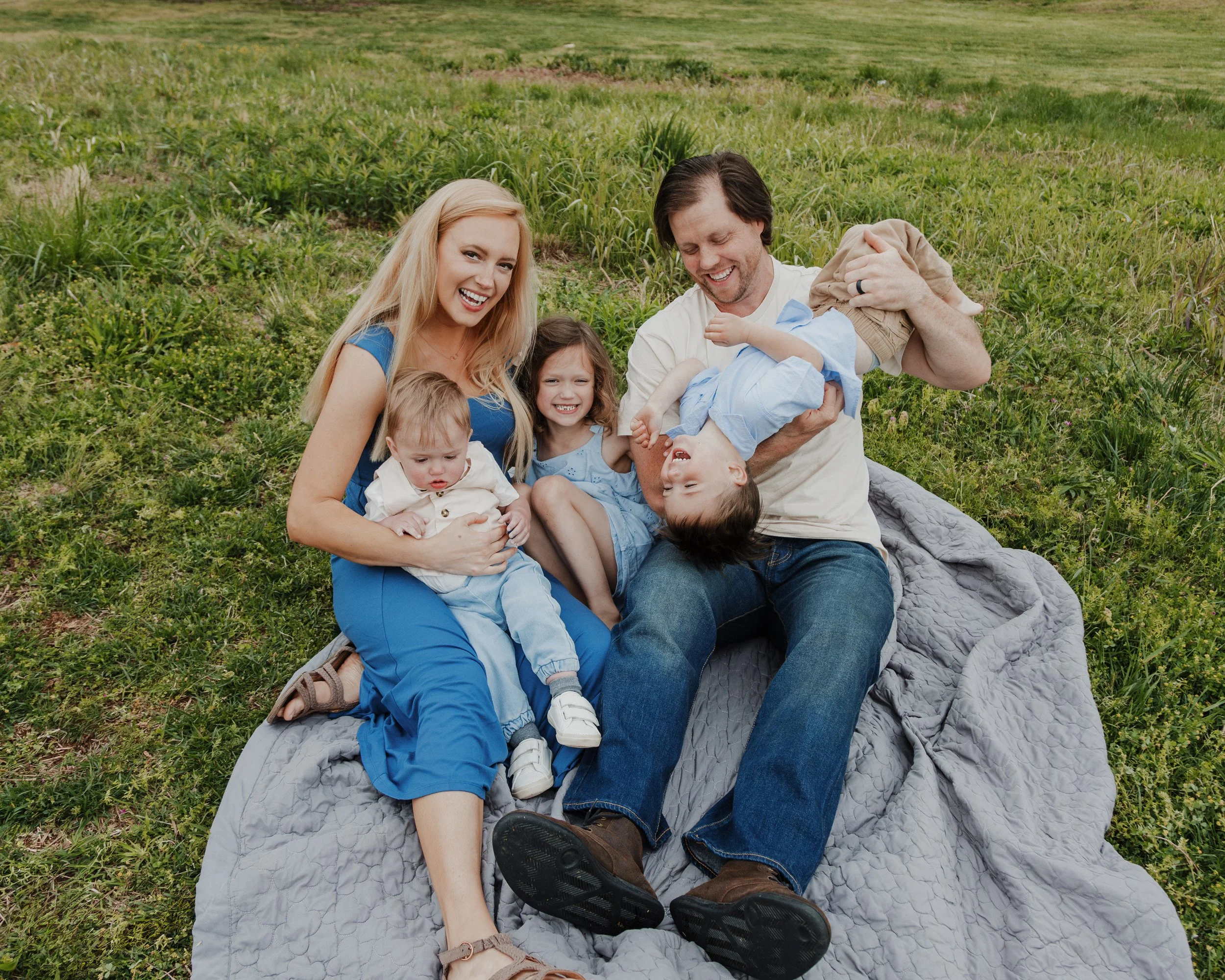Family with three young kids rough houses and smiles at the camera during a spring mini session at the NCMA in Raleigh.