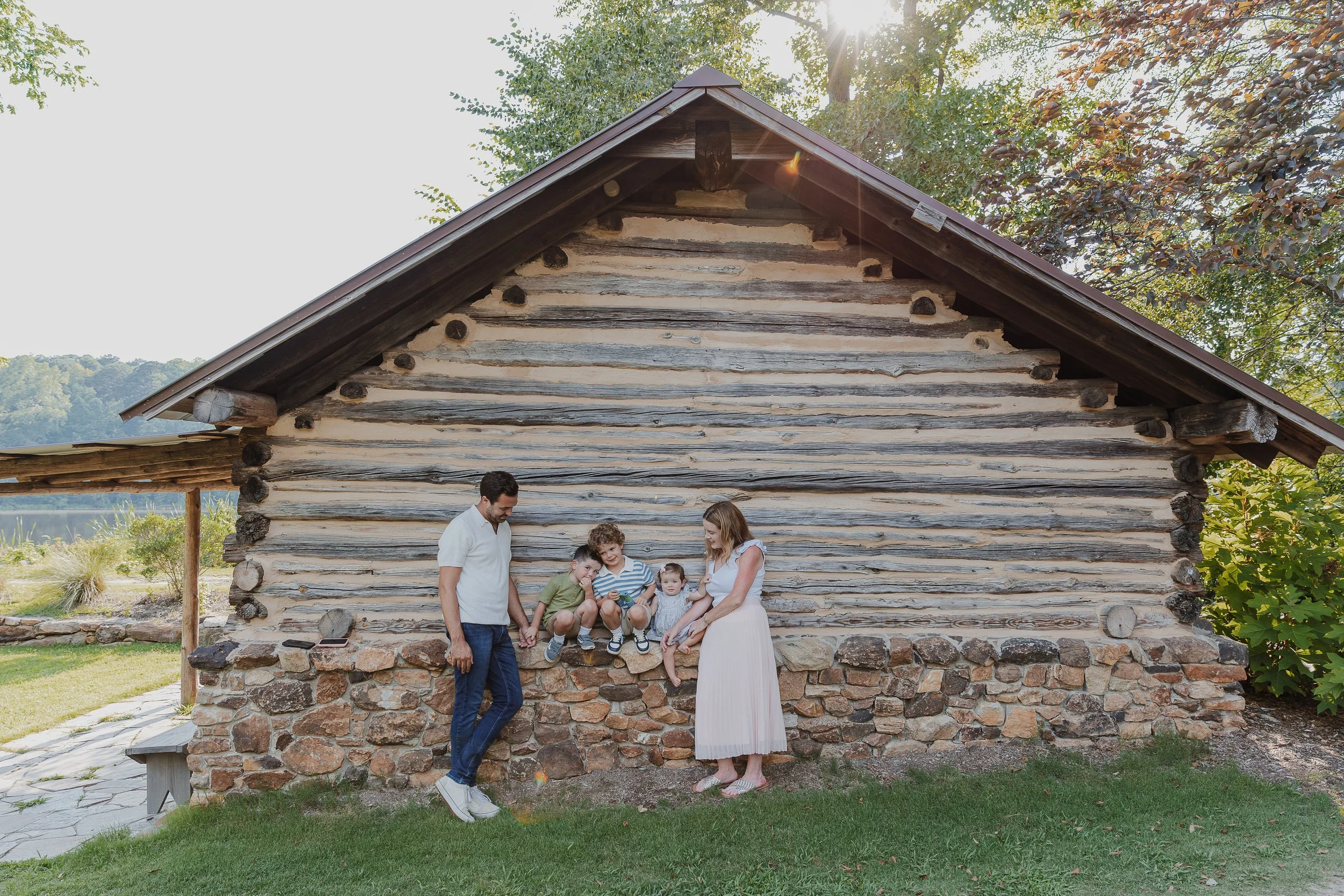 Parents and their three children sharing a quiet moment outside the historic log cabin at Historic Yates Mill County Park during a fall family photo session in Raleigh, NC.