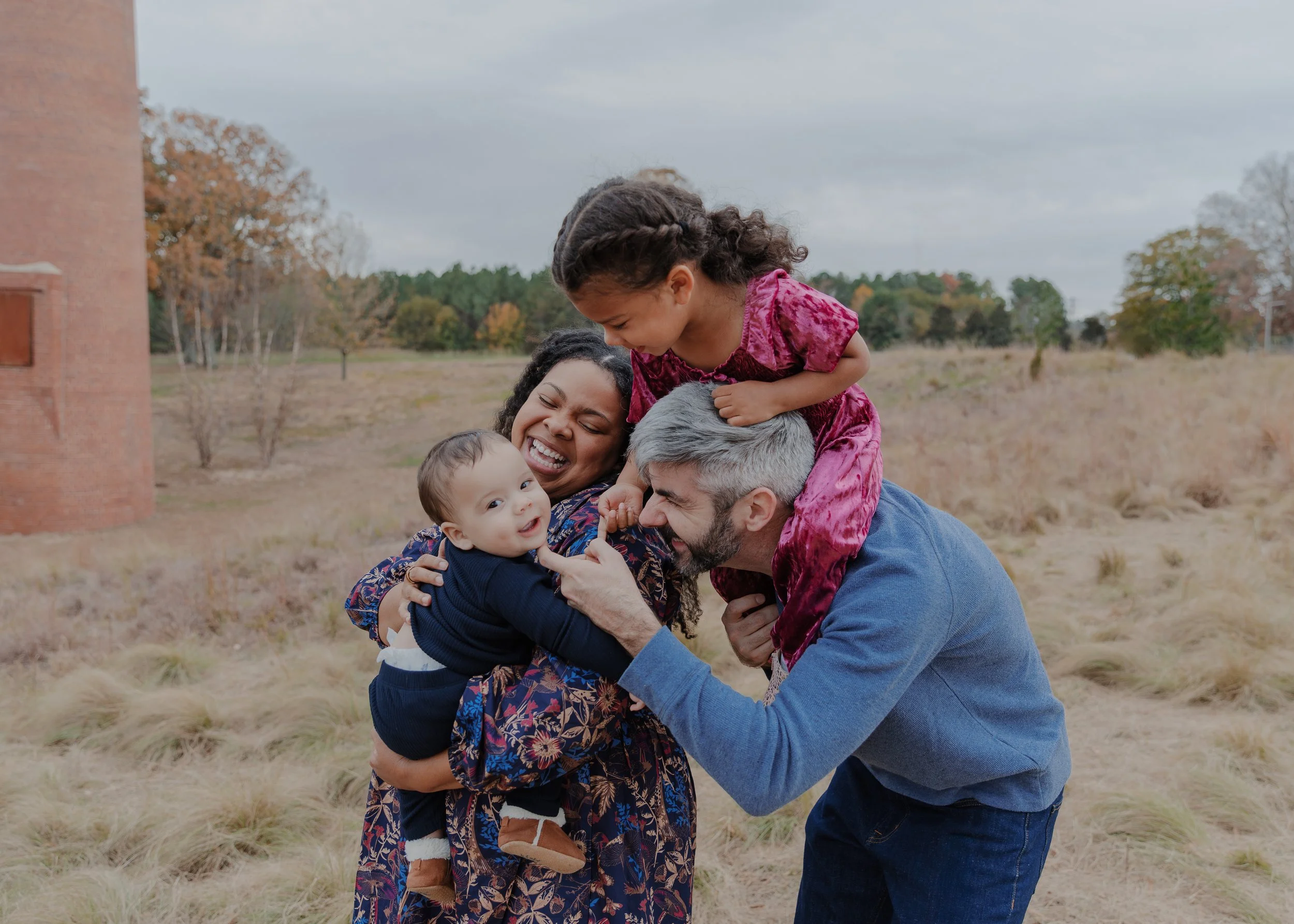 Family with a 3-year-old and baby laugh together during a family photography session at the North Carolina Museum of Art in Raleigh.