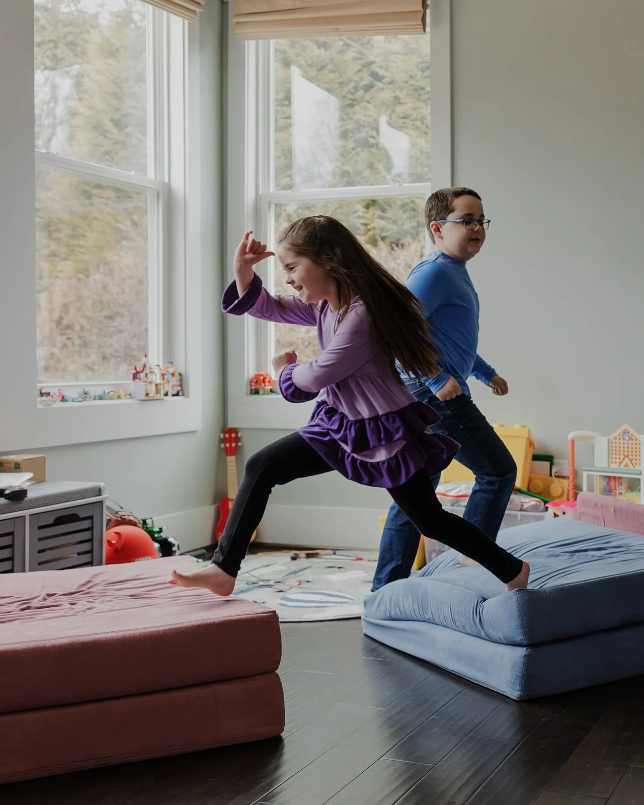 Child jumping between cushions while playing with her brother during a relaxed in-home neurodivergent family photo session in Wake Forest, NC.