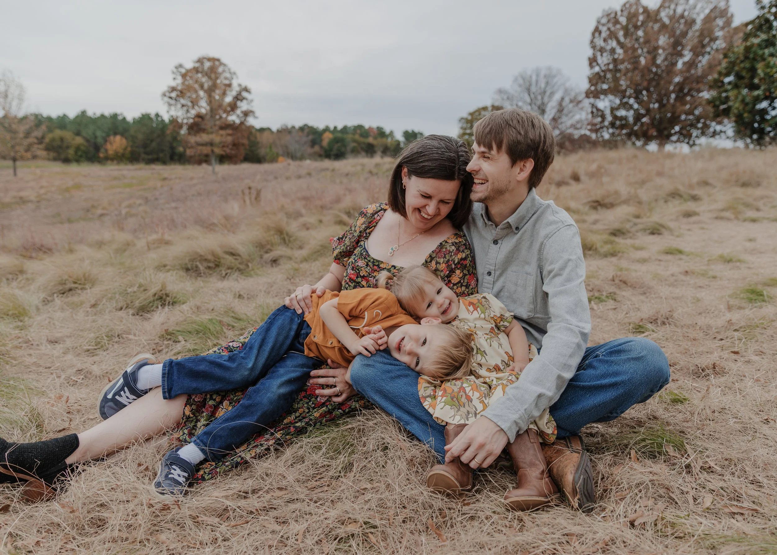 Parents laughing as their two young children play across their laps during a fall family photo session at the North Carolina Museum of Art in Raleigh, NC.