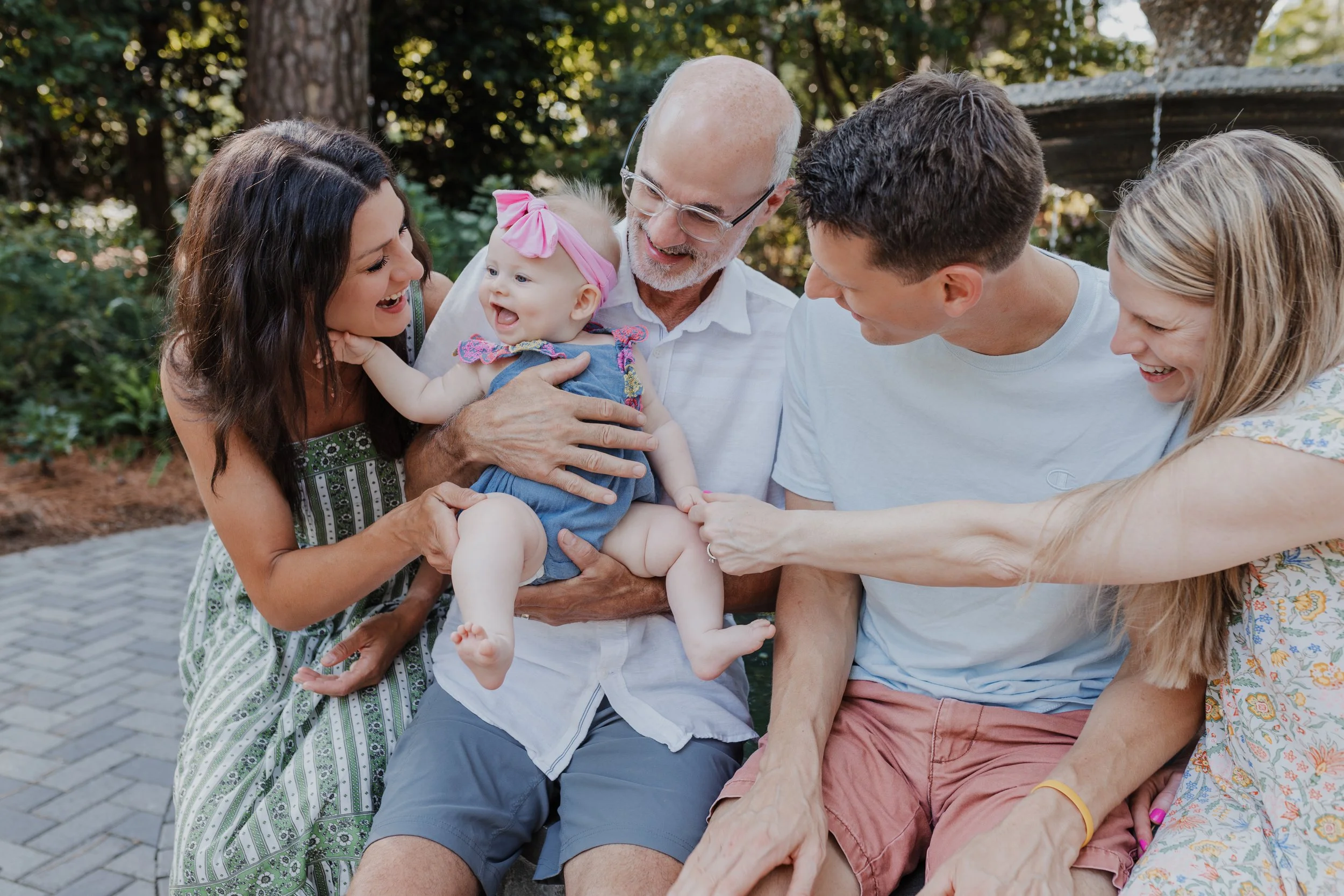 Family members tickle a laughing baby during an extended family photo session at the WRAL Azalea Gardens in Raleigh, NC.