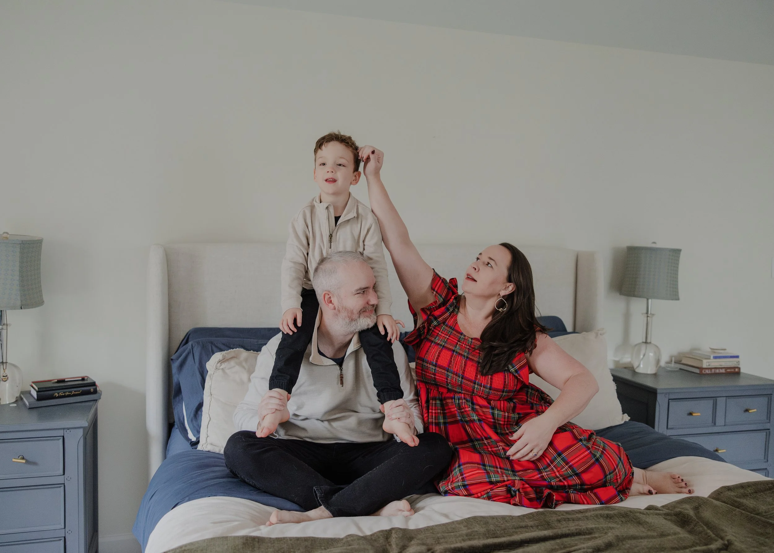 Mom, dad, and 4-year-old boy sit together on the bed in their Durham, NC home during a professional maternity photo session.