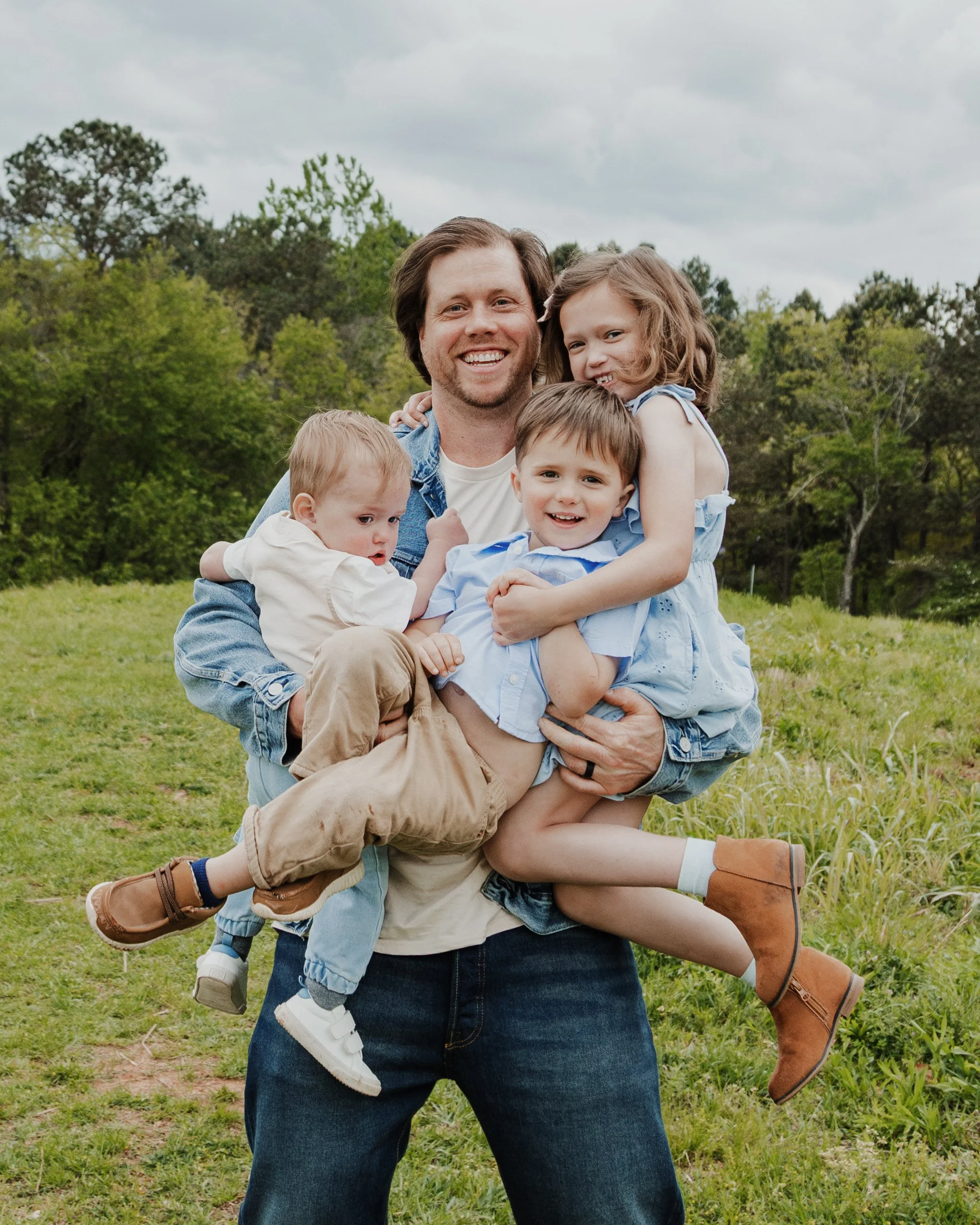 Dad holds three kids in his arms during a Father's Day mini photo session in Raleigh, North Carolina.