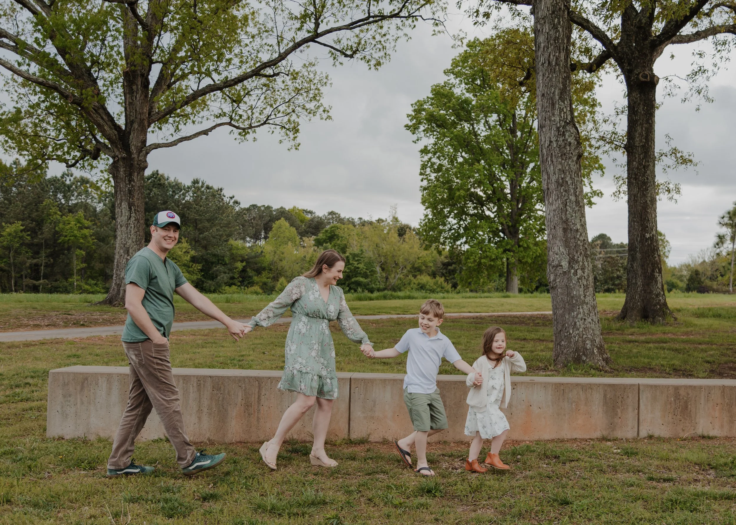 Family with a 10-year-old son and 8-year-old daughter with down syndrome walk together during springtime family photos at the NCMA Park in Raleigh, NC.