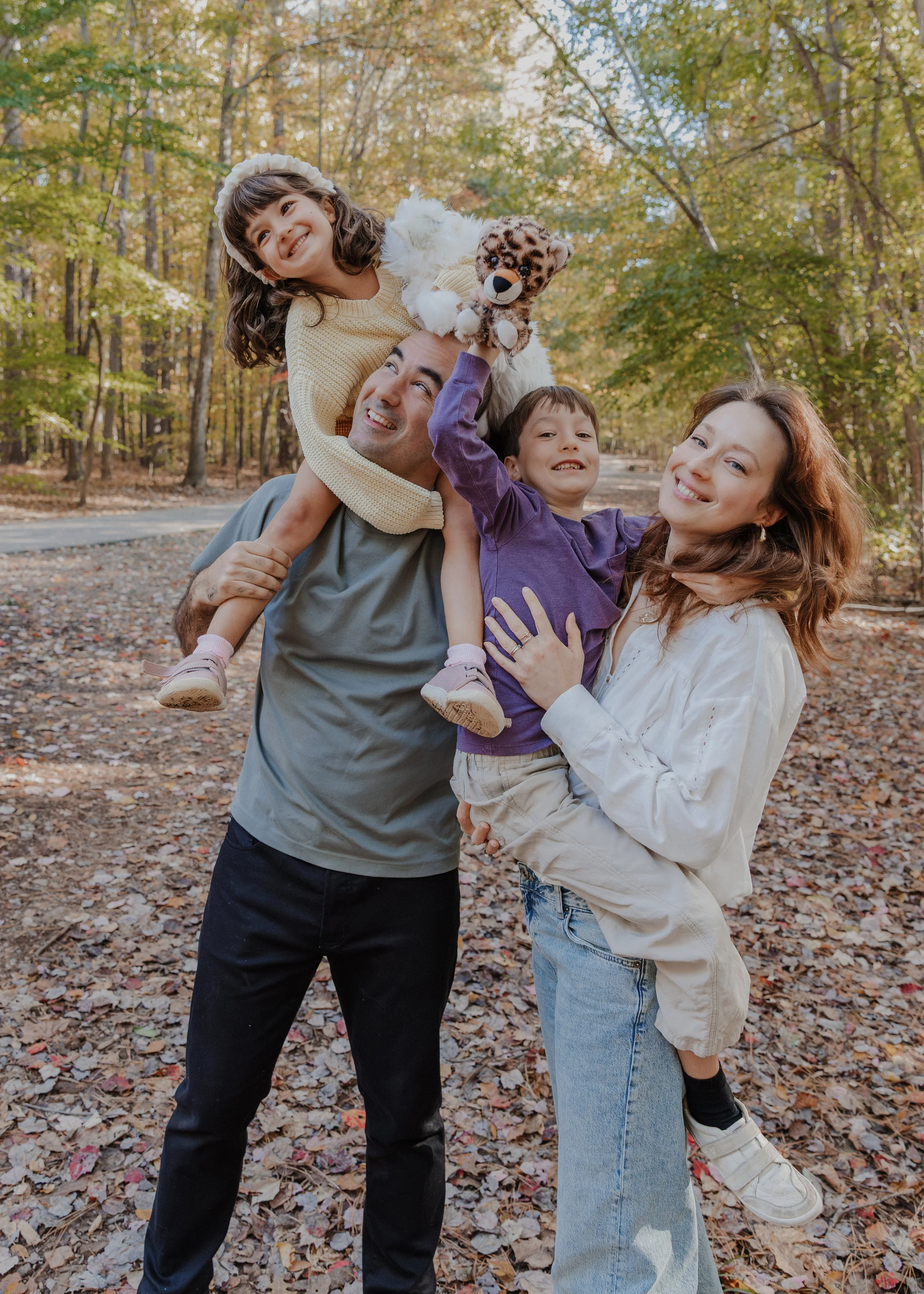 Family of four enjoying a playful fall family photo session at Bond Park in Cary, NC, surrounded by colorful autumn trees.