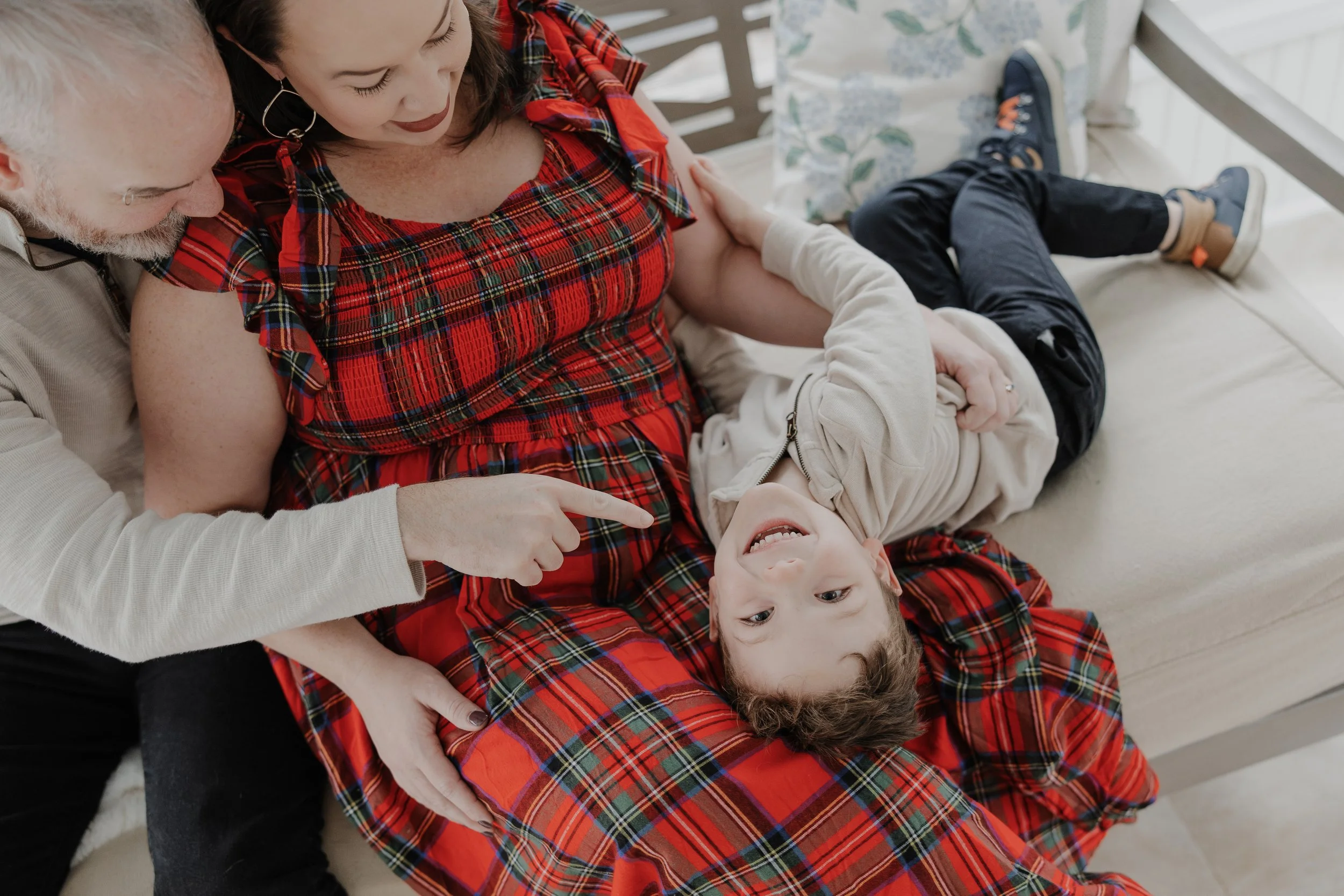 Family with 4-year-old boy sit on couch together during an at-home maternity photo session in Durham, NC.