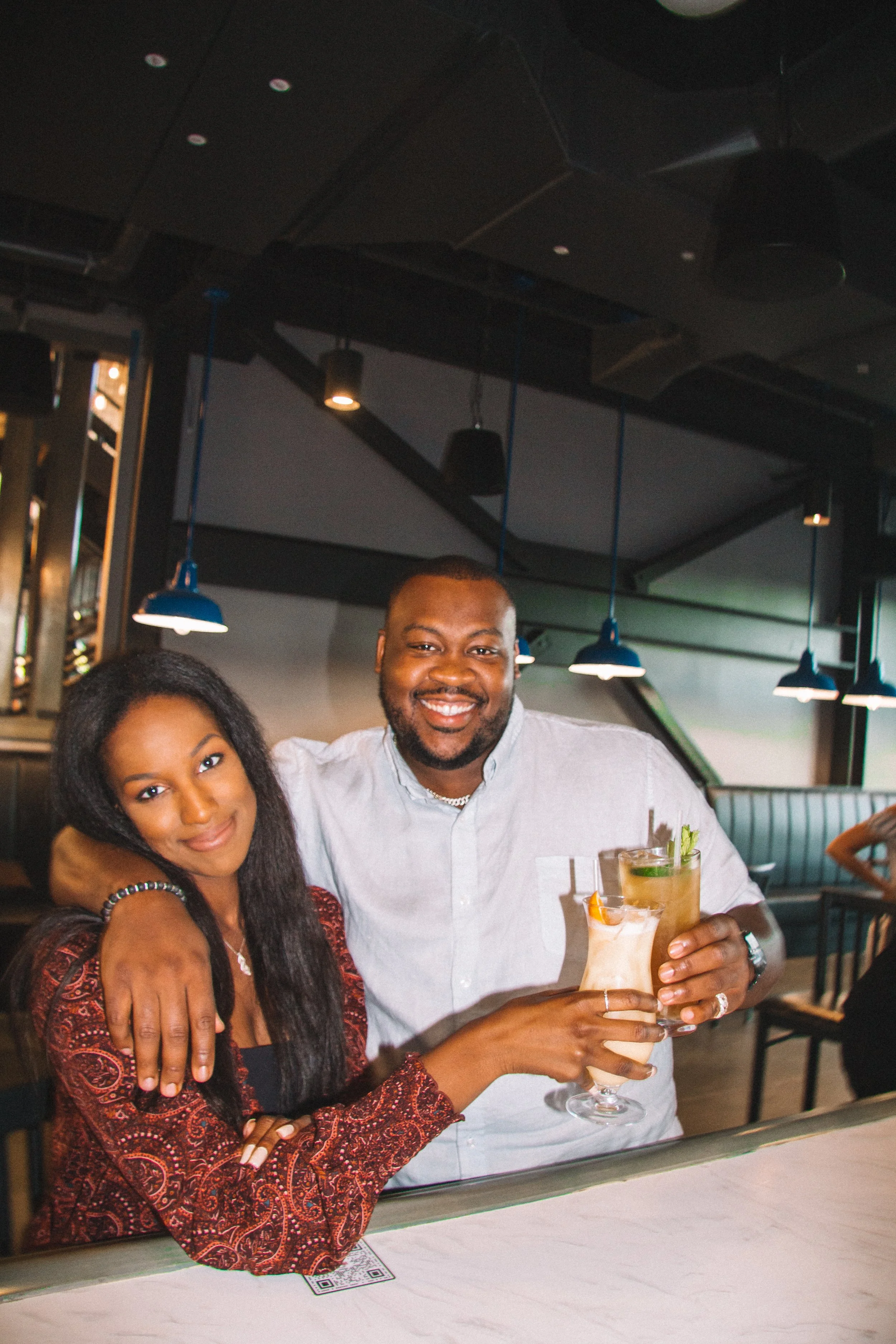 Two people smiling at the bar at Back 9 driving range, holding cocktail glasses.