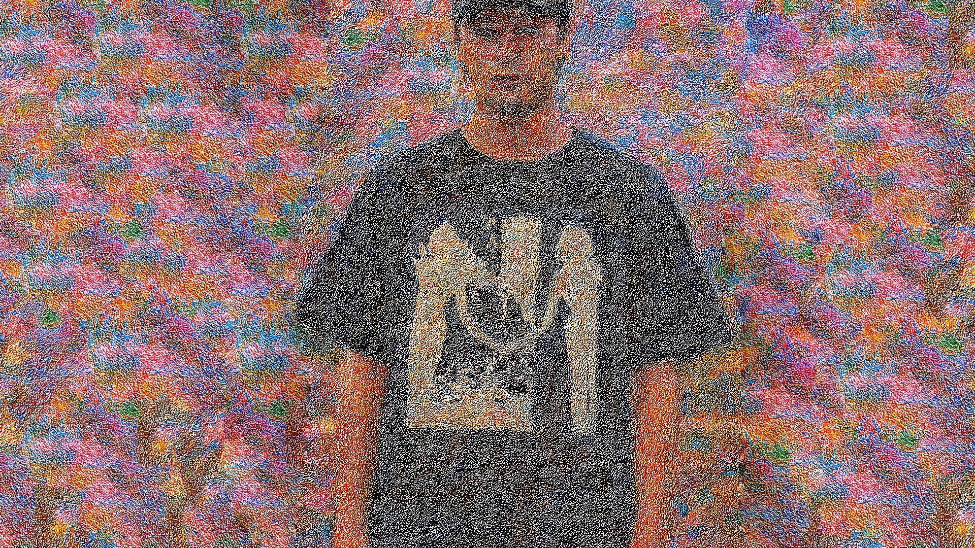 A young man wearing a black t-shirt with a graphic design, standing outdoors in front of a multicolored floral background.