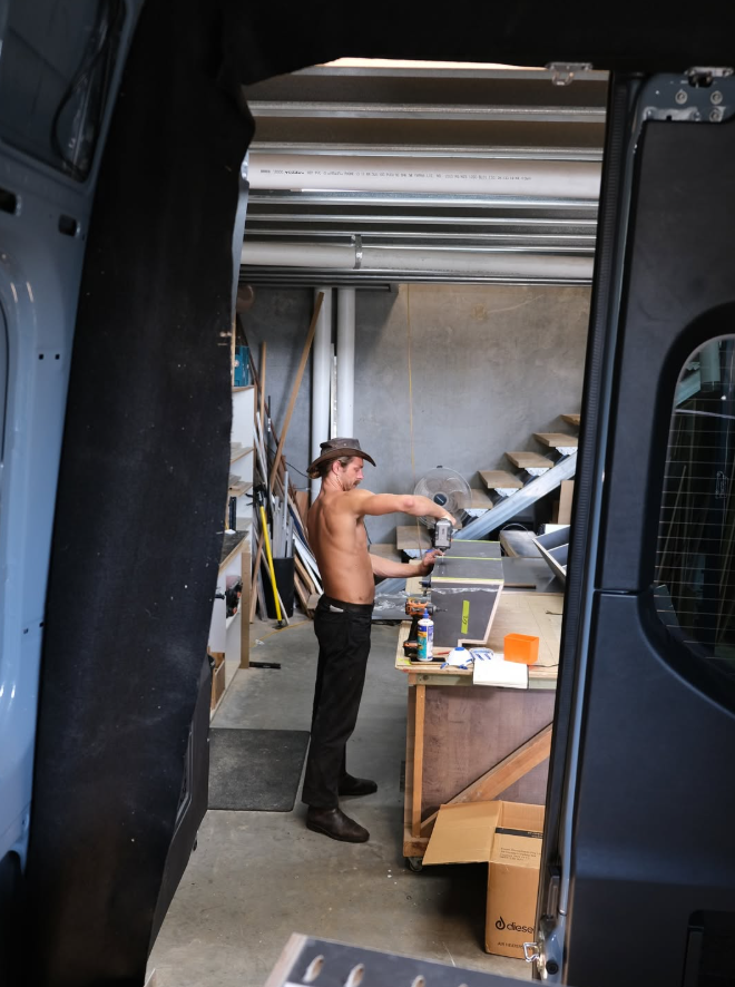 A shirtless man wearing a cowboy hat working with tools inside a garage or workshop.