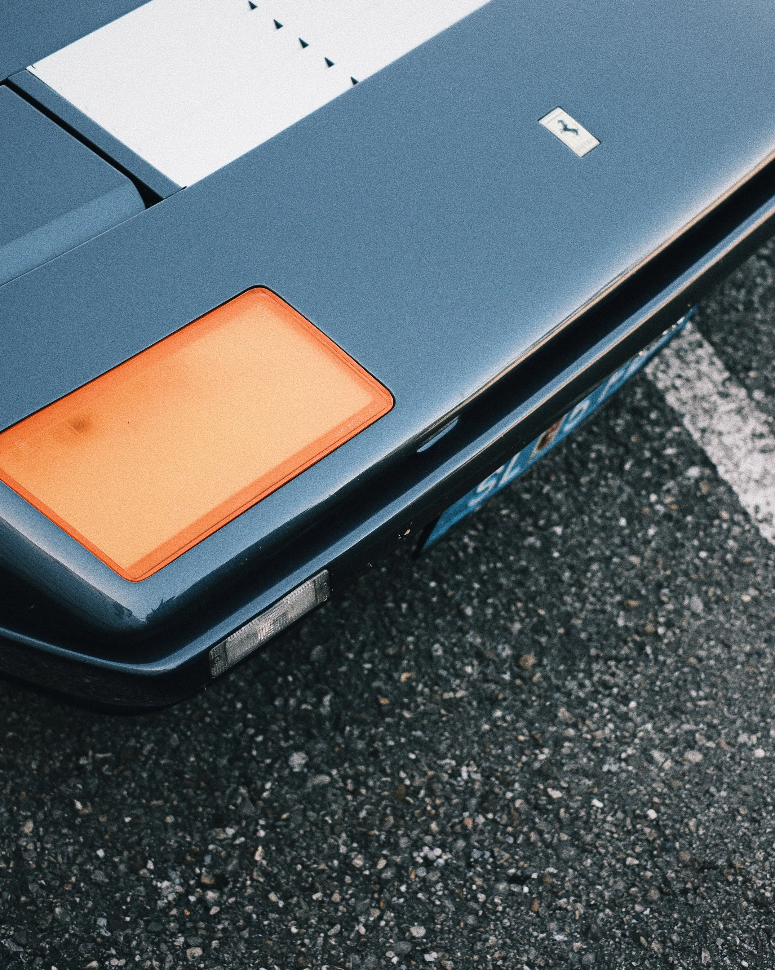 Close-up of the front corner of a black car on an asphalt road, showing an orange turn signal light.