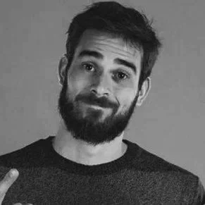 A man with a beard and short dark hair, giving a slight smile, in black and white.