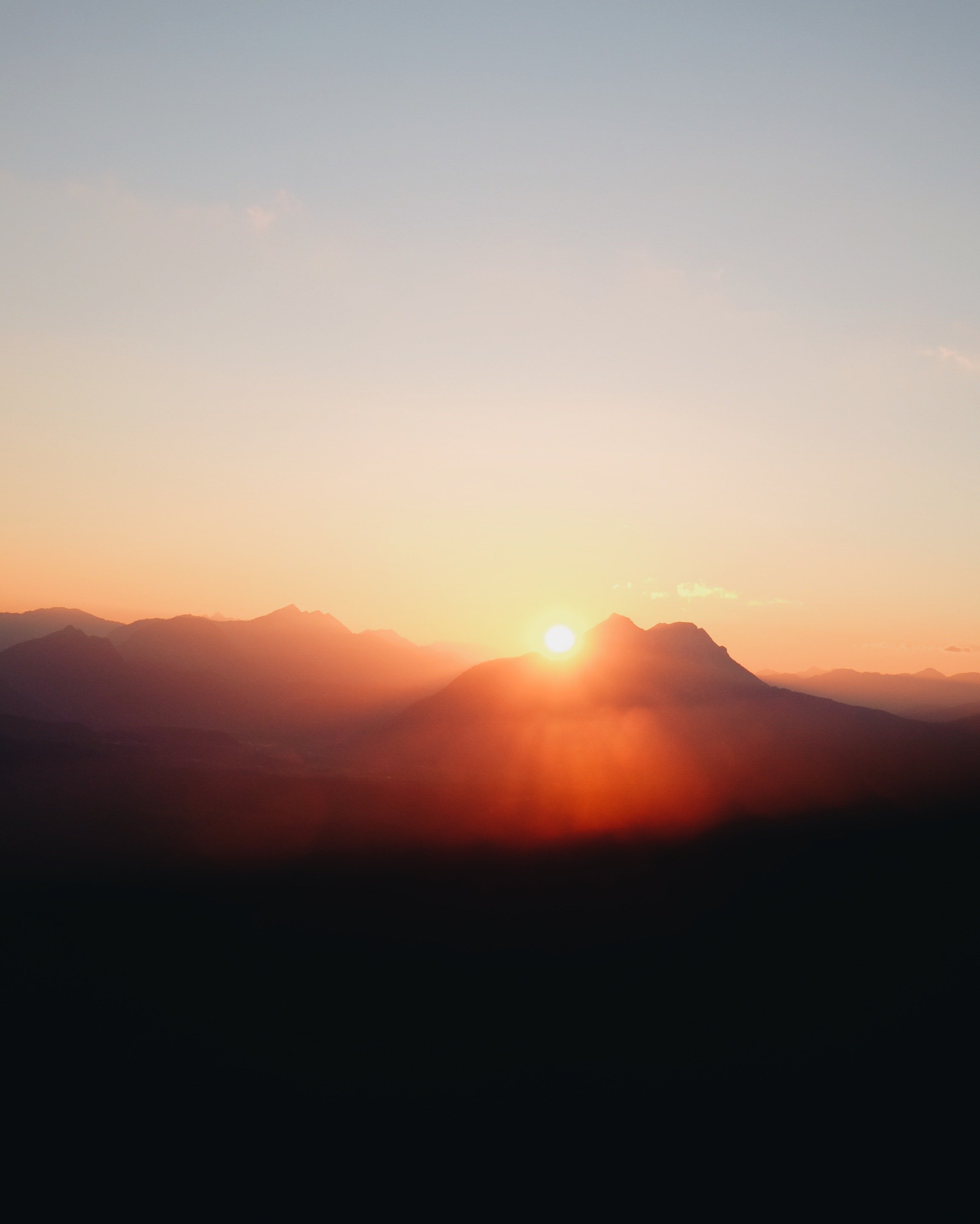 Sunset over a mountain range with the sun near the horizon, creating an orange glow in the sky.